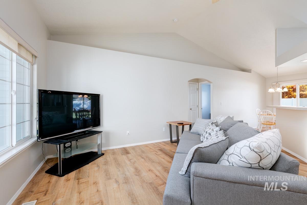 Living area featuring light wood-style flooring, arched walkways, lofted ceiling, and a chandelier