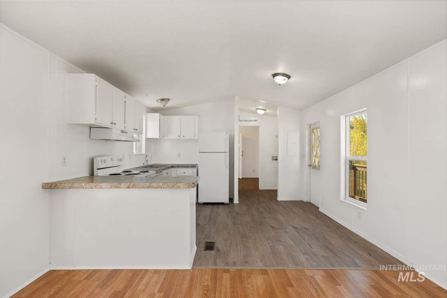 Kitchen featuring white cabinetry, white appliances, light wood-type flooring, light countertops, and under cabinet range hood