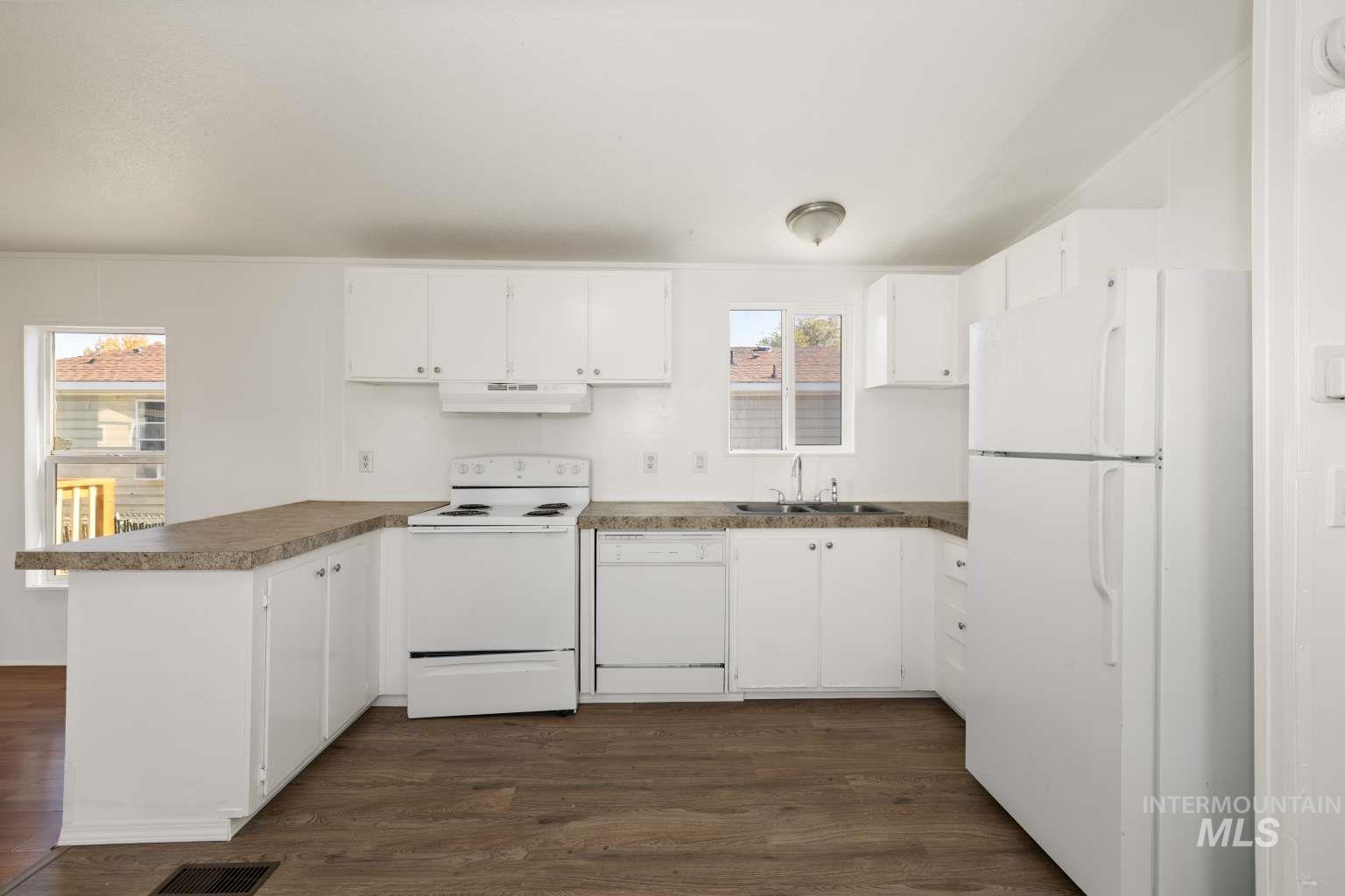 Kitchen with white appliances, white cabinets, dark wood-type flooring, and dark countertops