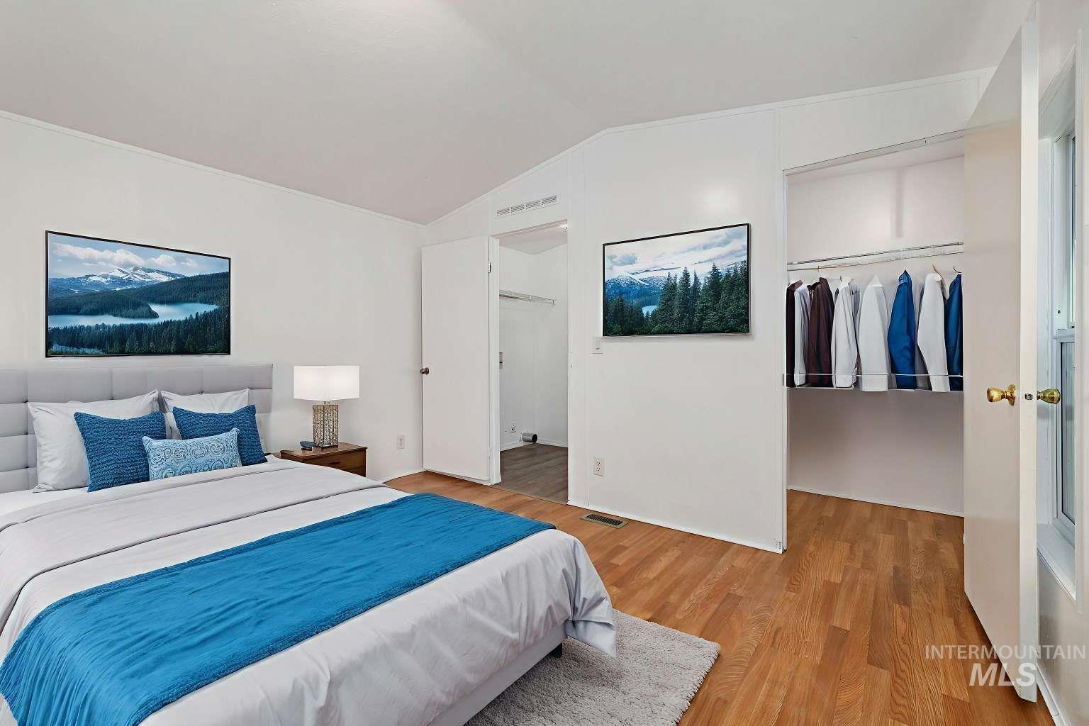 Bedroom featuring a walk in closet, wood finished floors, and lofted ceiling