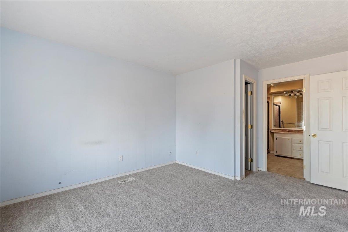 Unfurnished bedroom with carpet, ensuite bath, and a textured ceiling