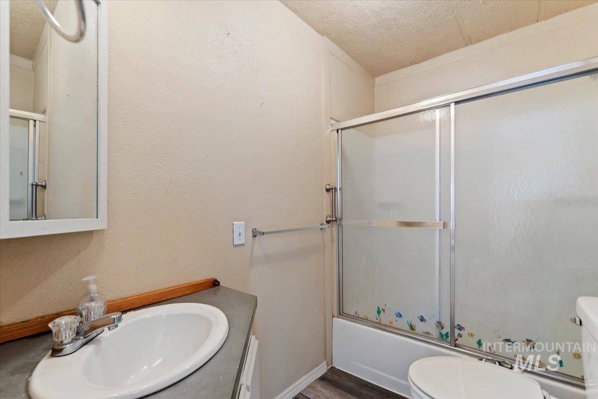 Bathroom featuring vanity, a textured ceiling, bath / shower combo with glass door, and a textured wall