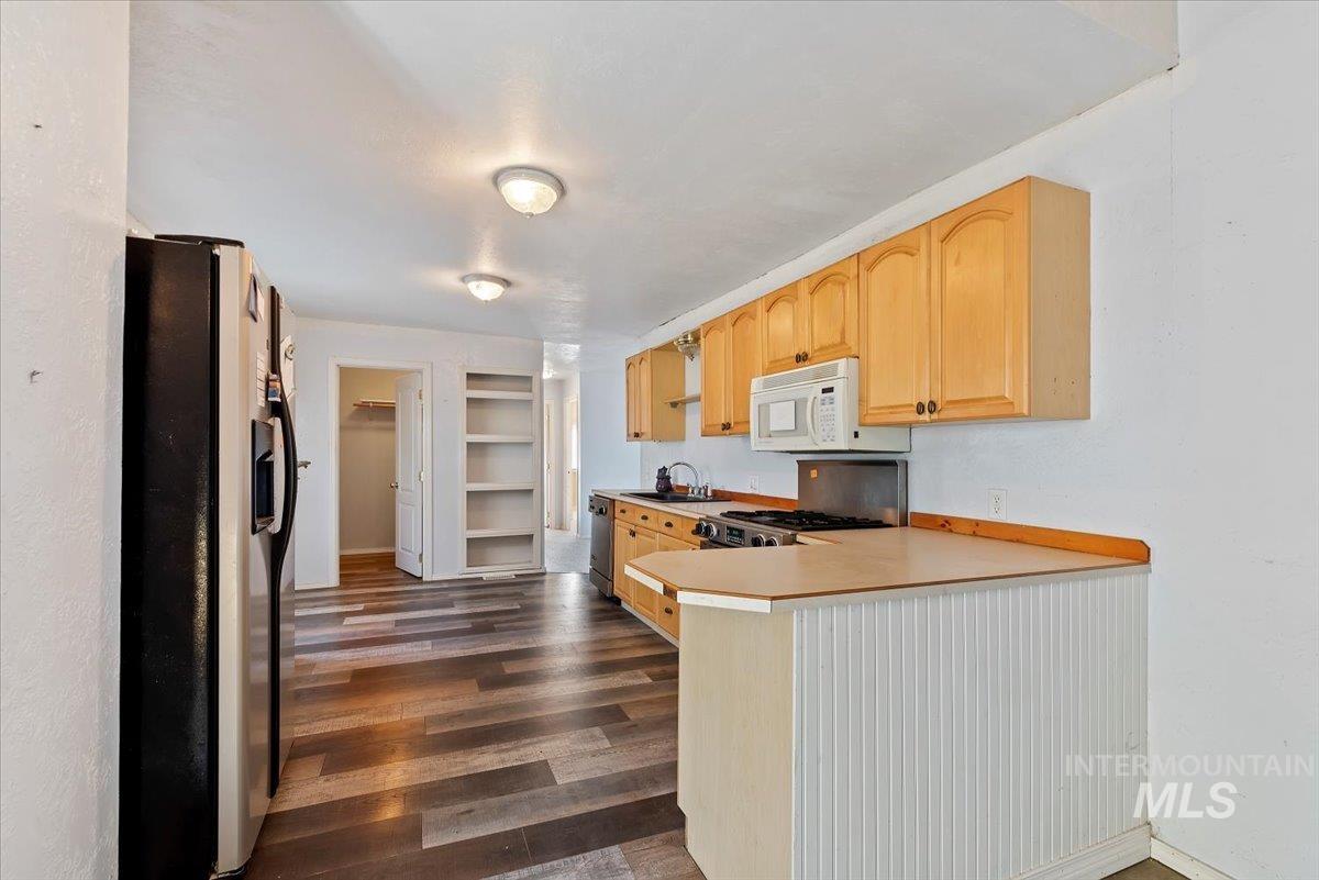 Kitchen featuring light brown cabinetry, light countertops, stainless steel appliances, and a peninsula