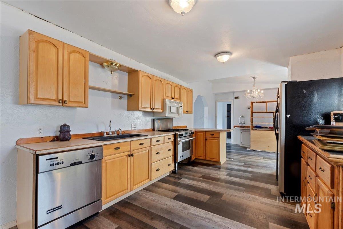 Kitchen with open shelves, stainless steel appliances, light brown cabinetry, dark wood-style floors, and a chandelier