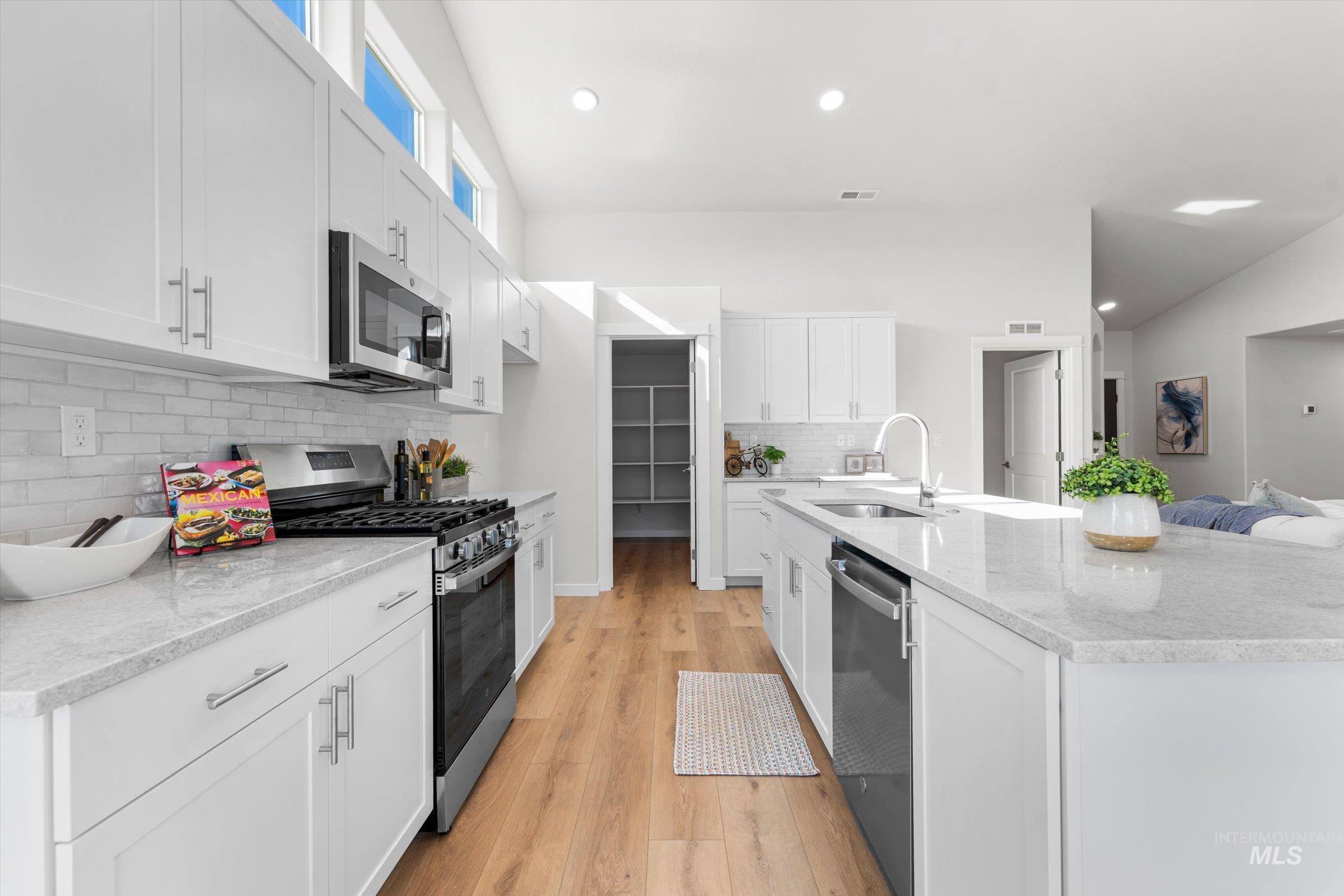 Kitchen featuring stainless steel appliances, light wood finished floors, decorative backsplash, light stone counters, and white cabinetry