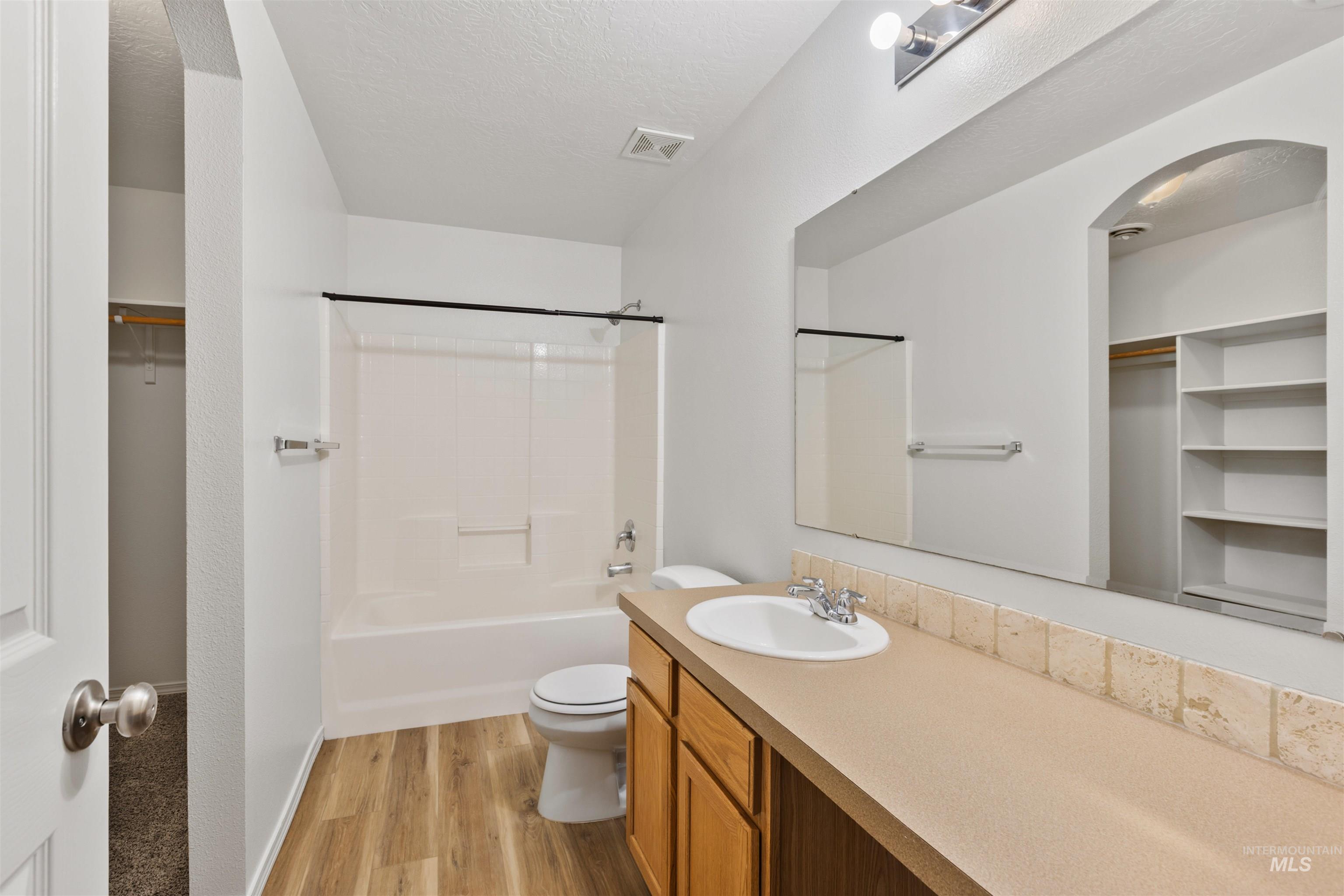 Full bathroom featuring a walk in closet, light wood finished floors, shower / tub combination, vanity, and a textured ceiling