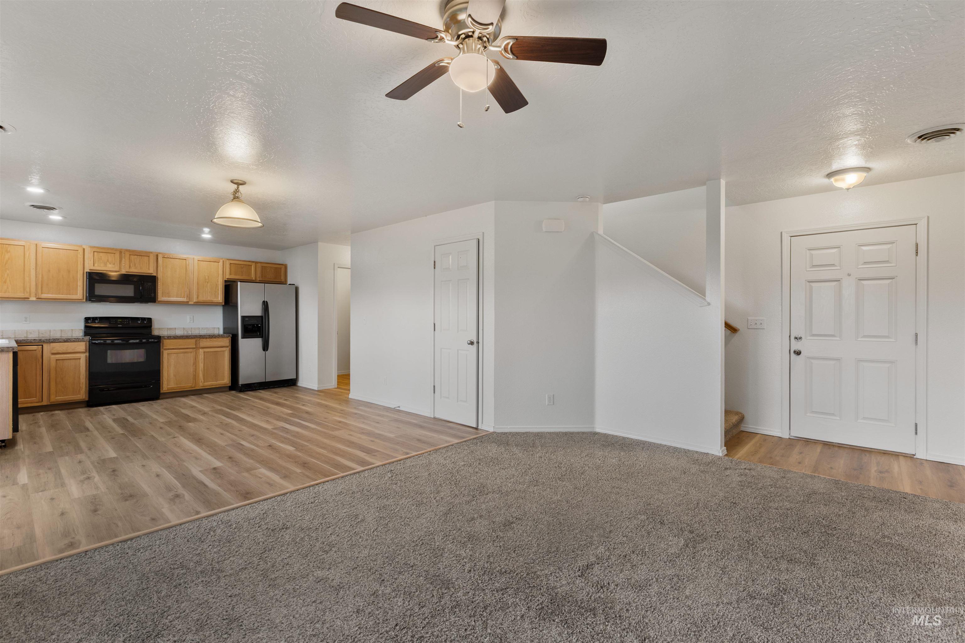 Kitchen with light colored carpet, black appliances, a textured ceiling, and light wood-style flooring