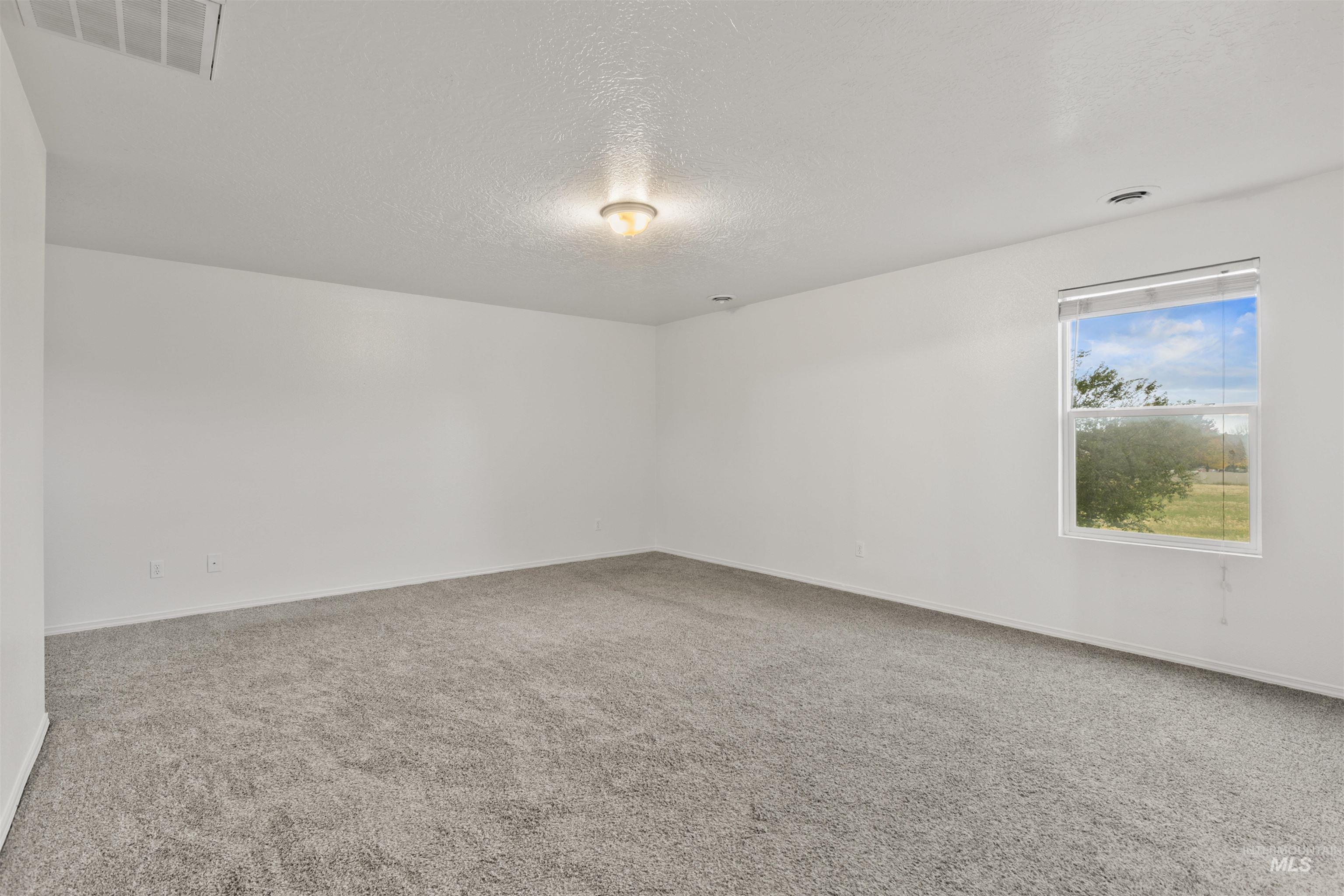 Empty room with a textured ceiling and light colored carpet
