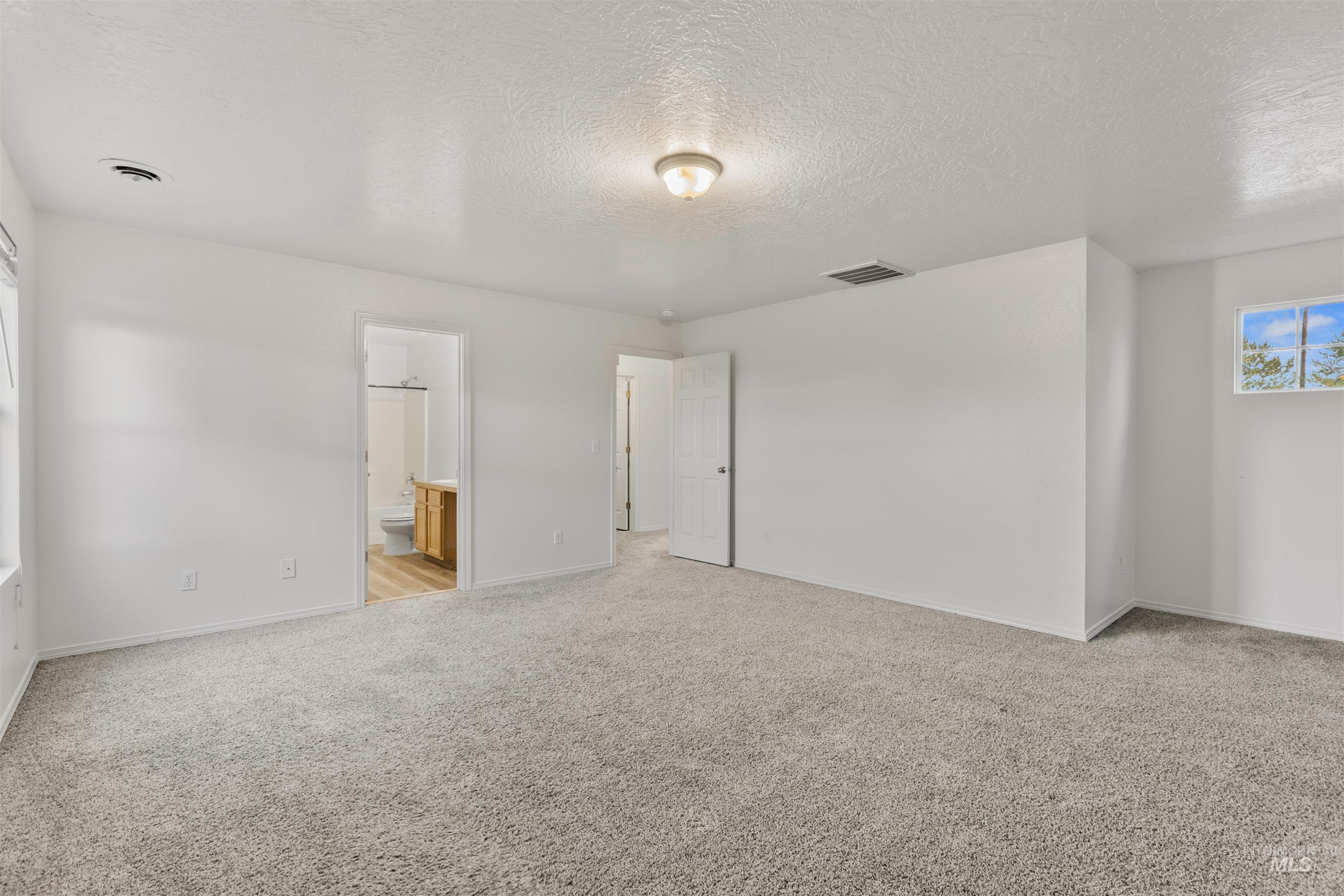 Unfurnished bedroom with a textured ceiling, light carpet, and connected bathroom