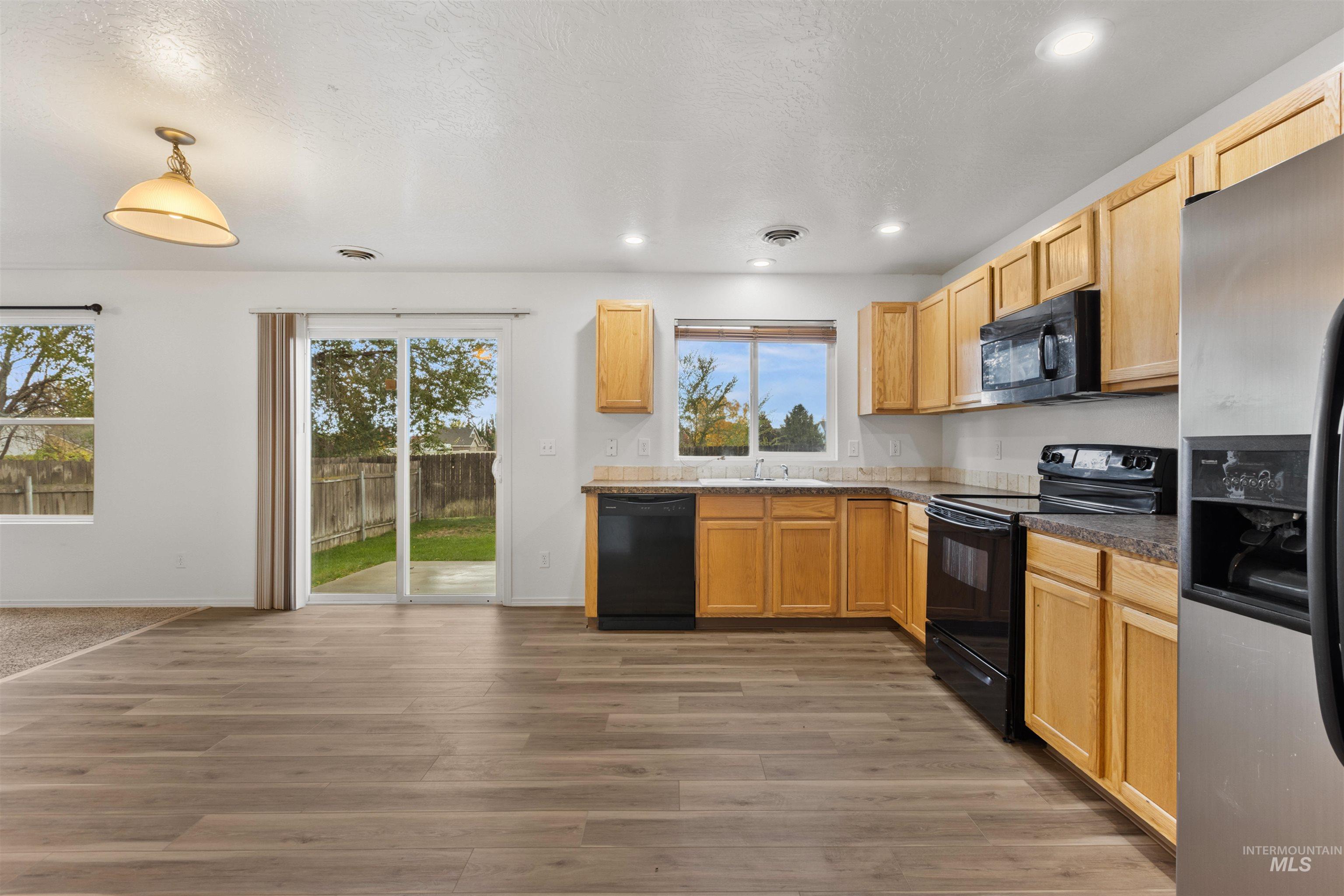 Kitchen featuring black appliances, light brown cabinets, dark wood finished floors, a textured ceiling, and recessed lighting