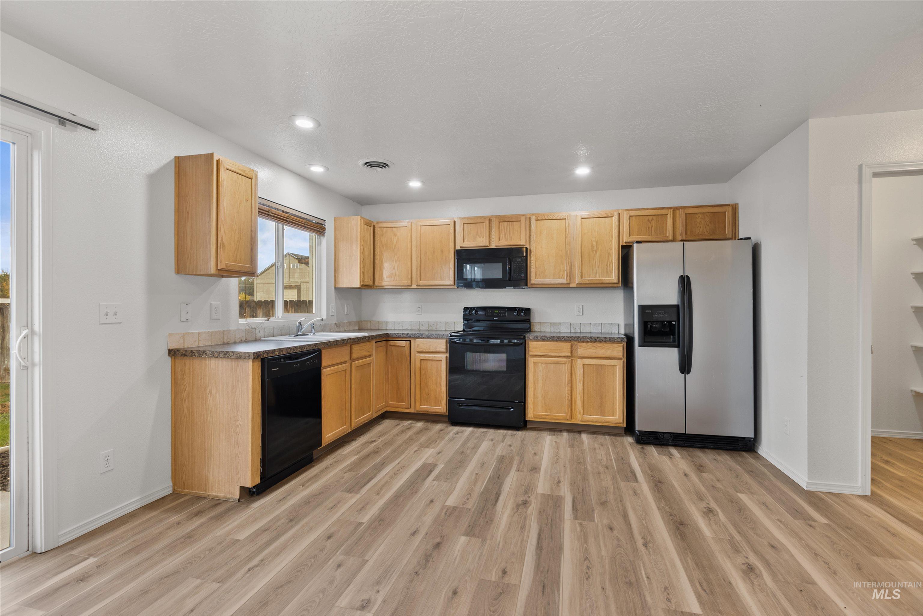 Kitchen with black appliances, light wood-style flooring, recessed lighting, light brown cabinetry, and dark countertops