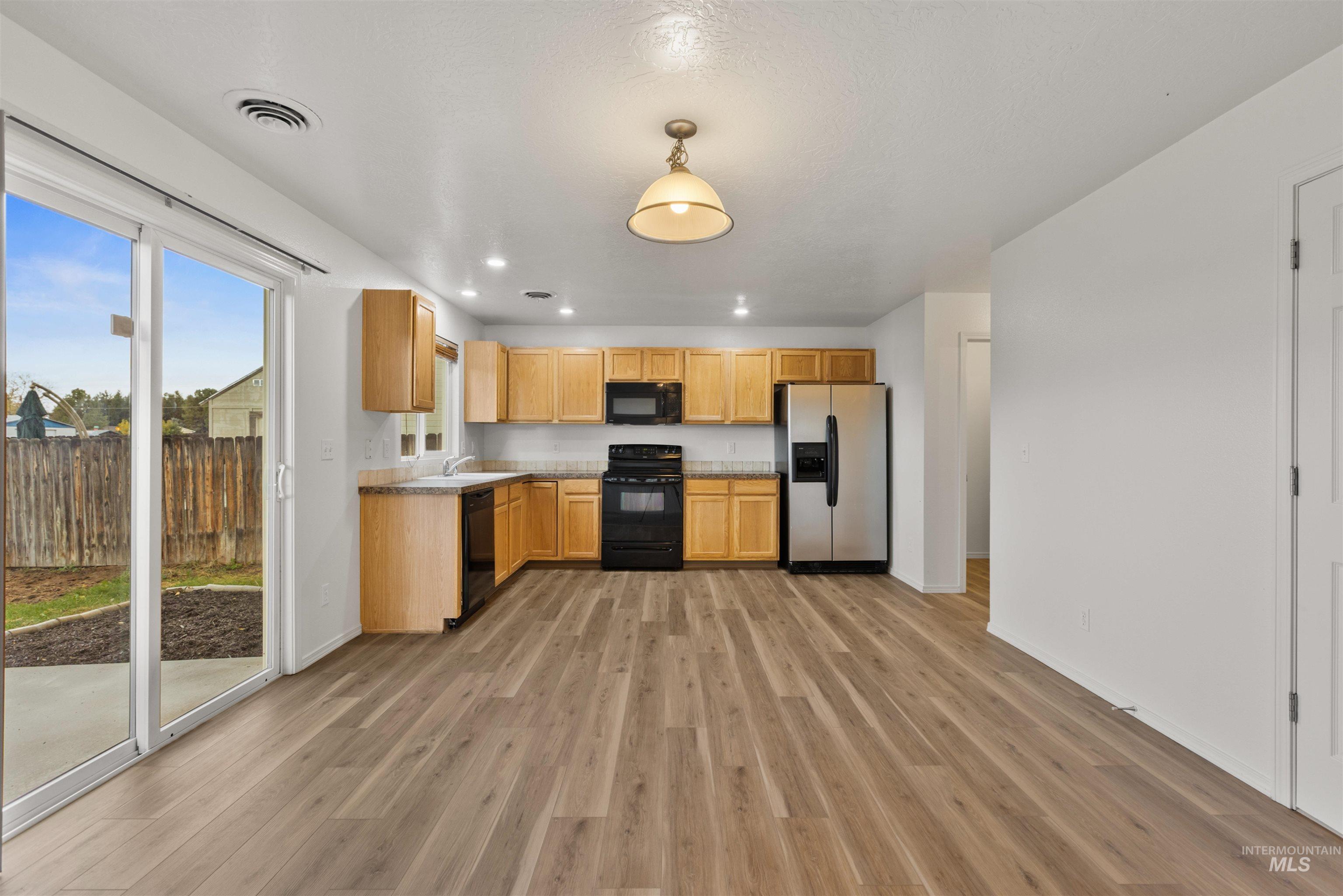 Kitchen featuring black appliances, light countertops, light brown cabinets, light wood finished floors, and recessed lighting