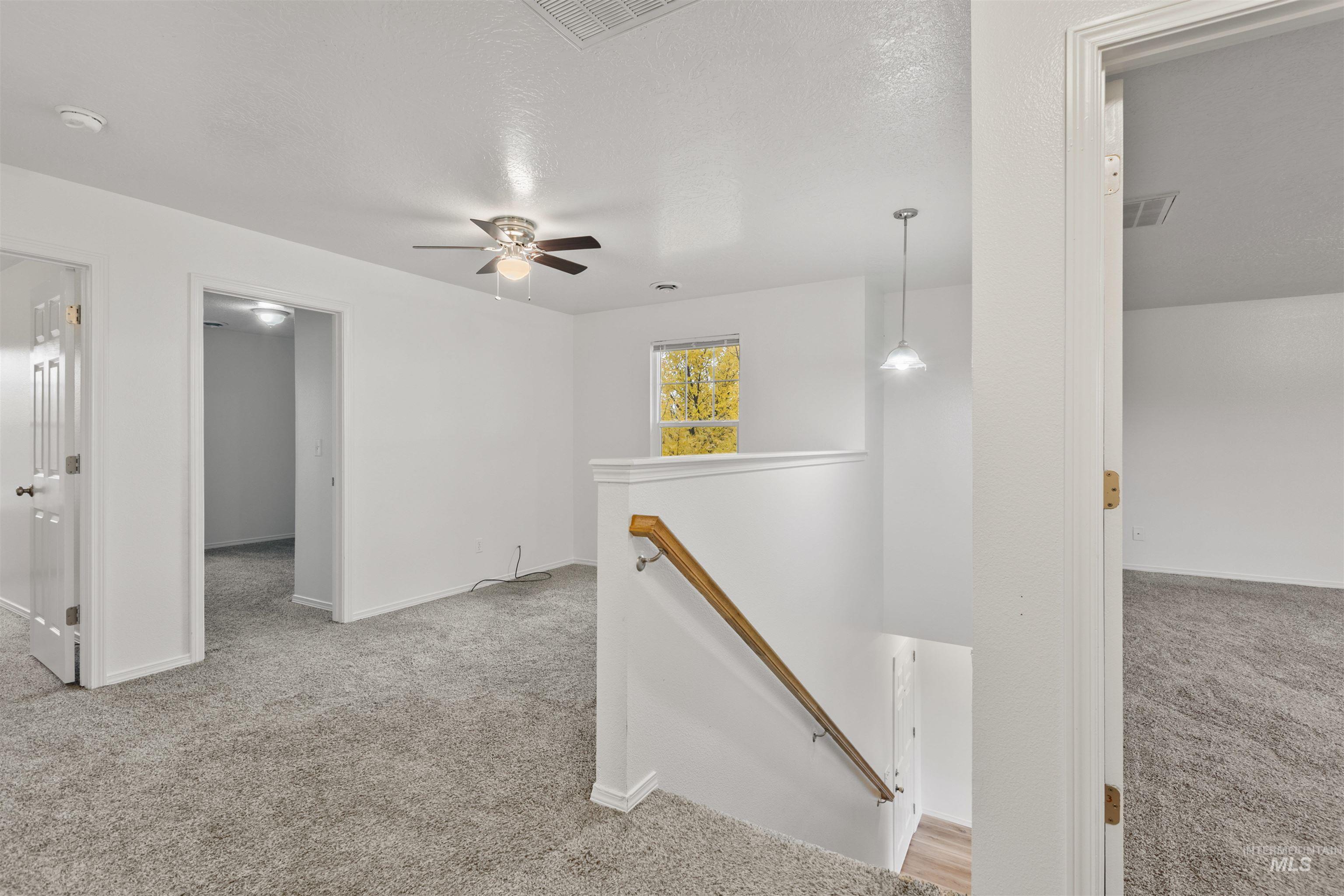 Hallway with light colored carpet, an upstairs landing, and a textured ceiling