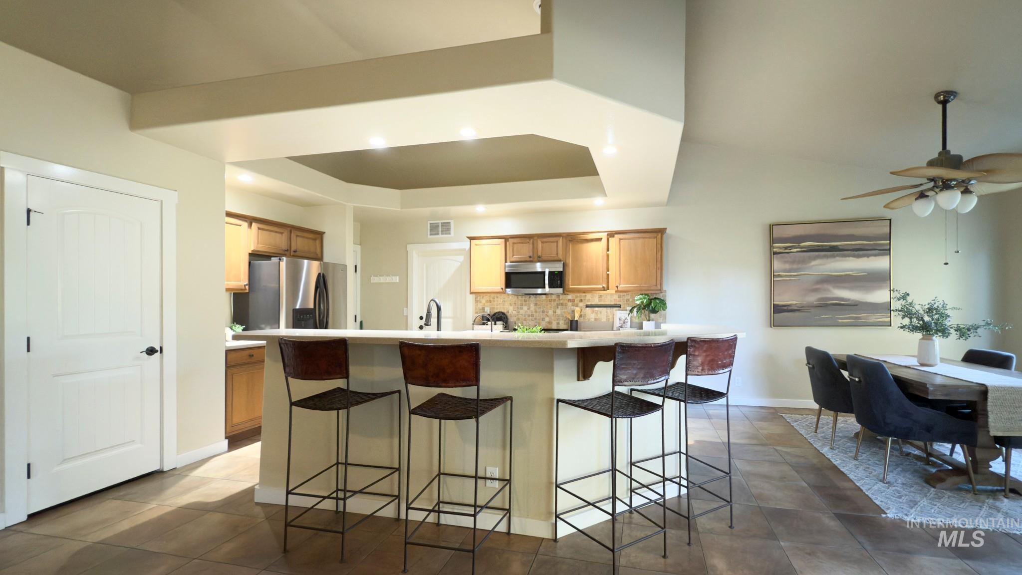 Kitchen with a kitchen bar, decorative backsplash, light countertops, a center island with sink, and stainless steel appliances