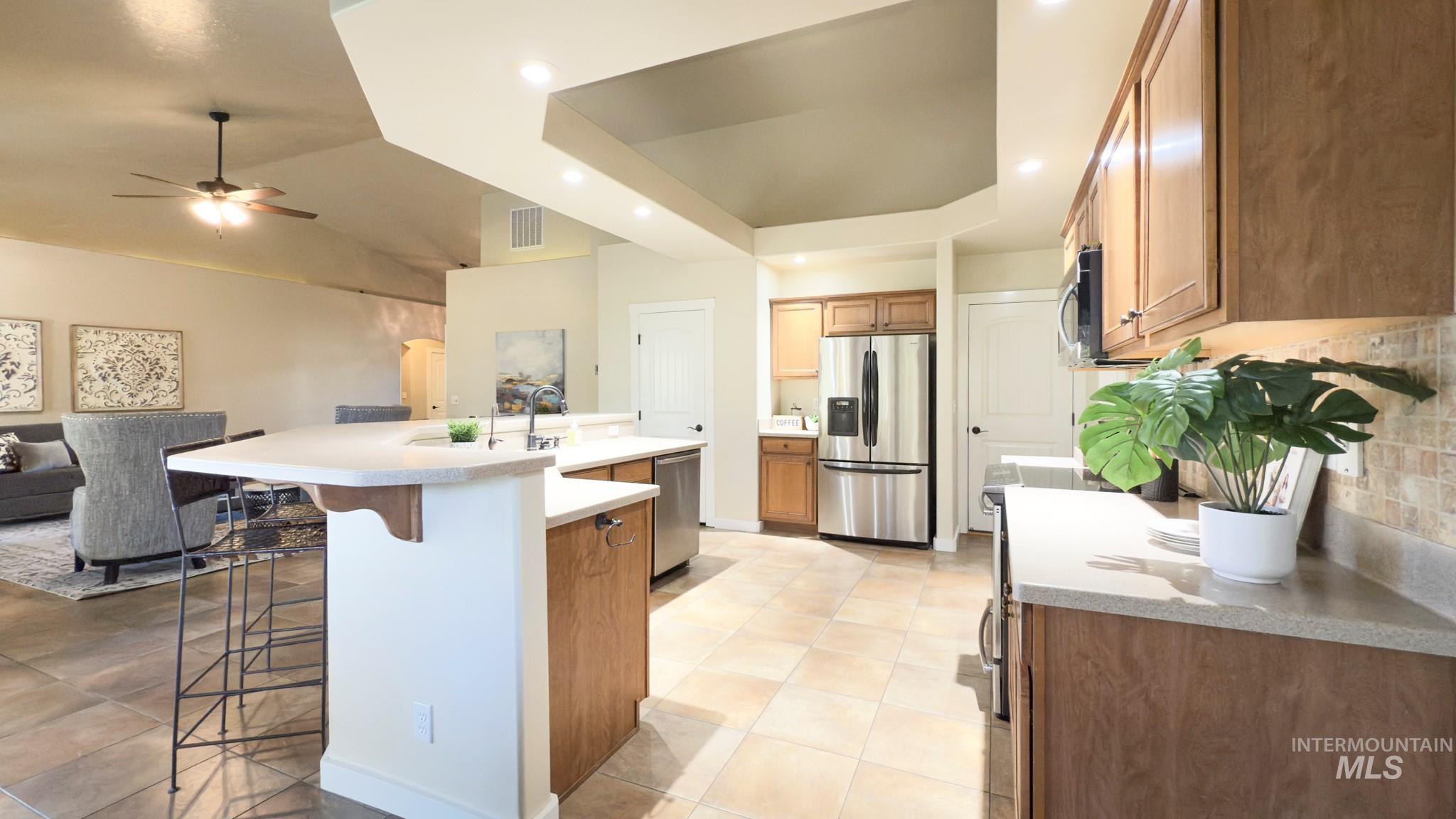 Kitchen featuring brown cabinets, a kitchen breakfast bar, stainless steel appliances, a spacious island, and backsplash