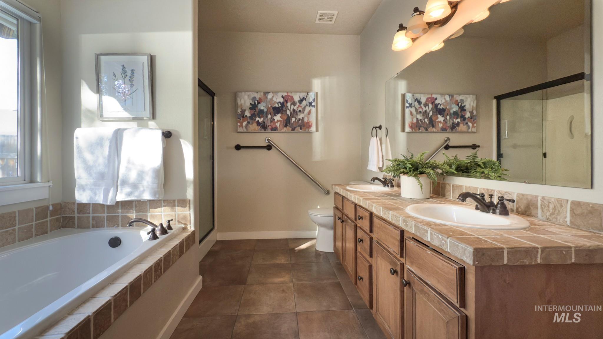 Full bath featuring double vanity, a stall shower, a garden tub, and dark tile patterned flooring
