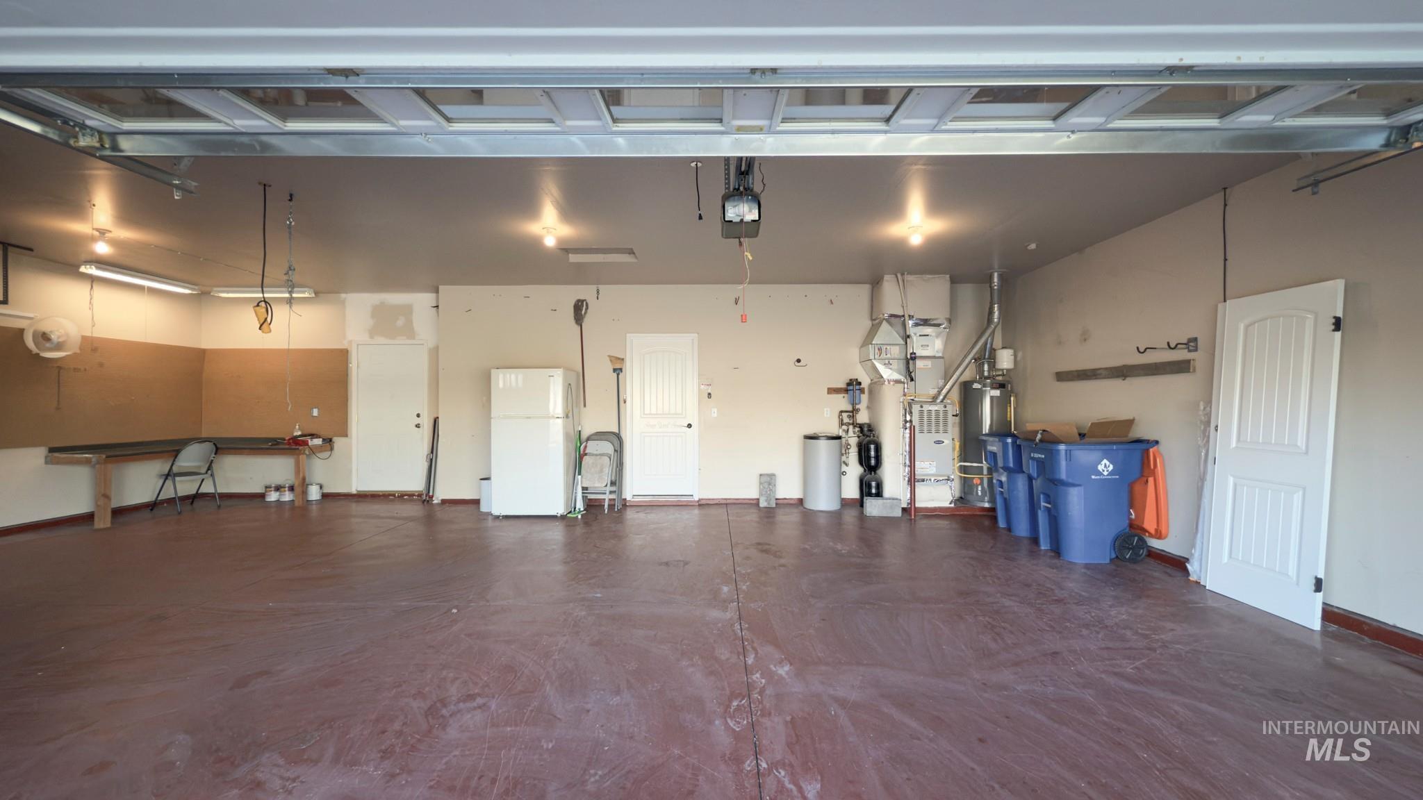 Garage with freestanding refrigerator, gas water heater, a garage door opener, and heating unit