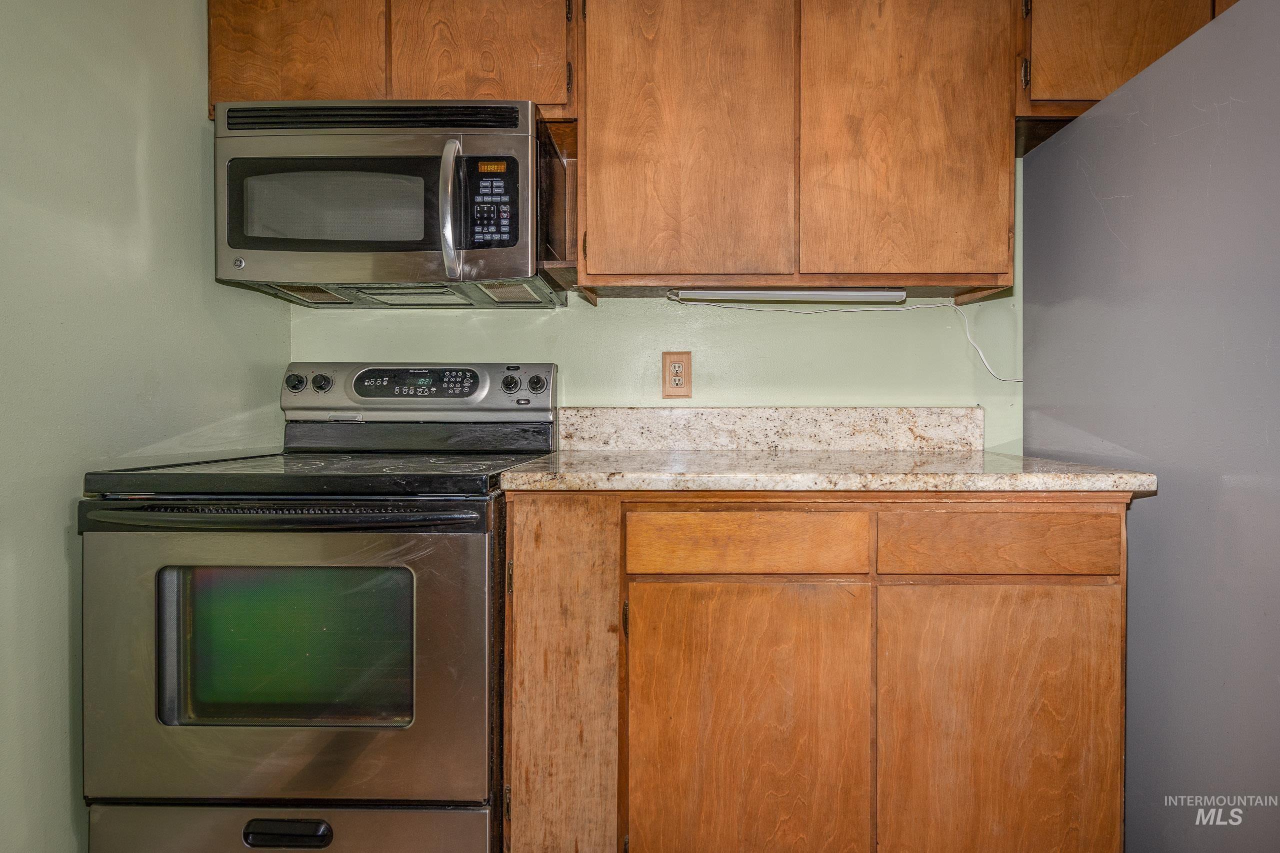 Kitchen featuring stainless steel appliances, brown cabinets, and light stone countertops
