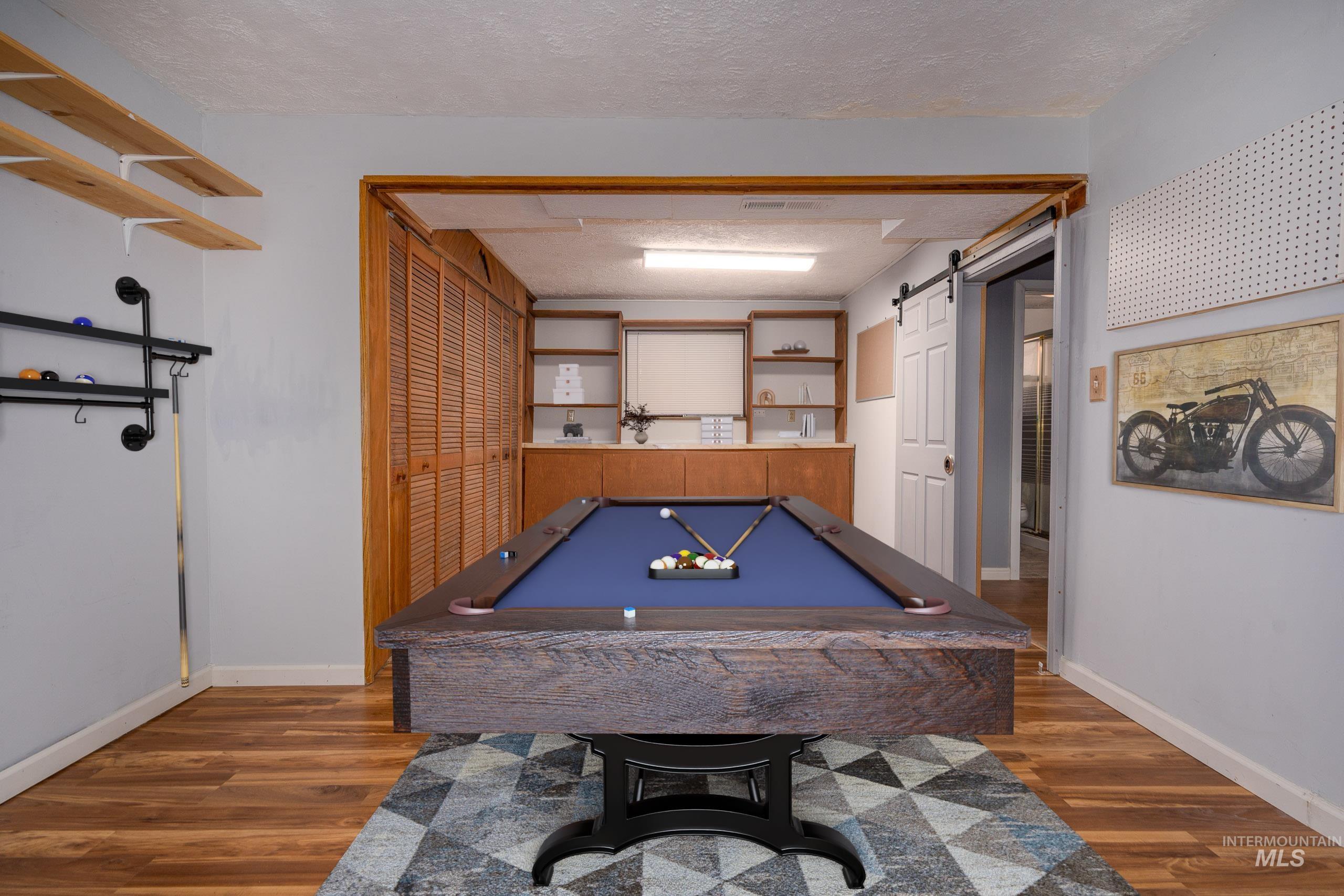 Playroom with a barn door, a textured ceiling, pool table, and dark wood-type flooring