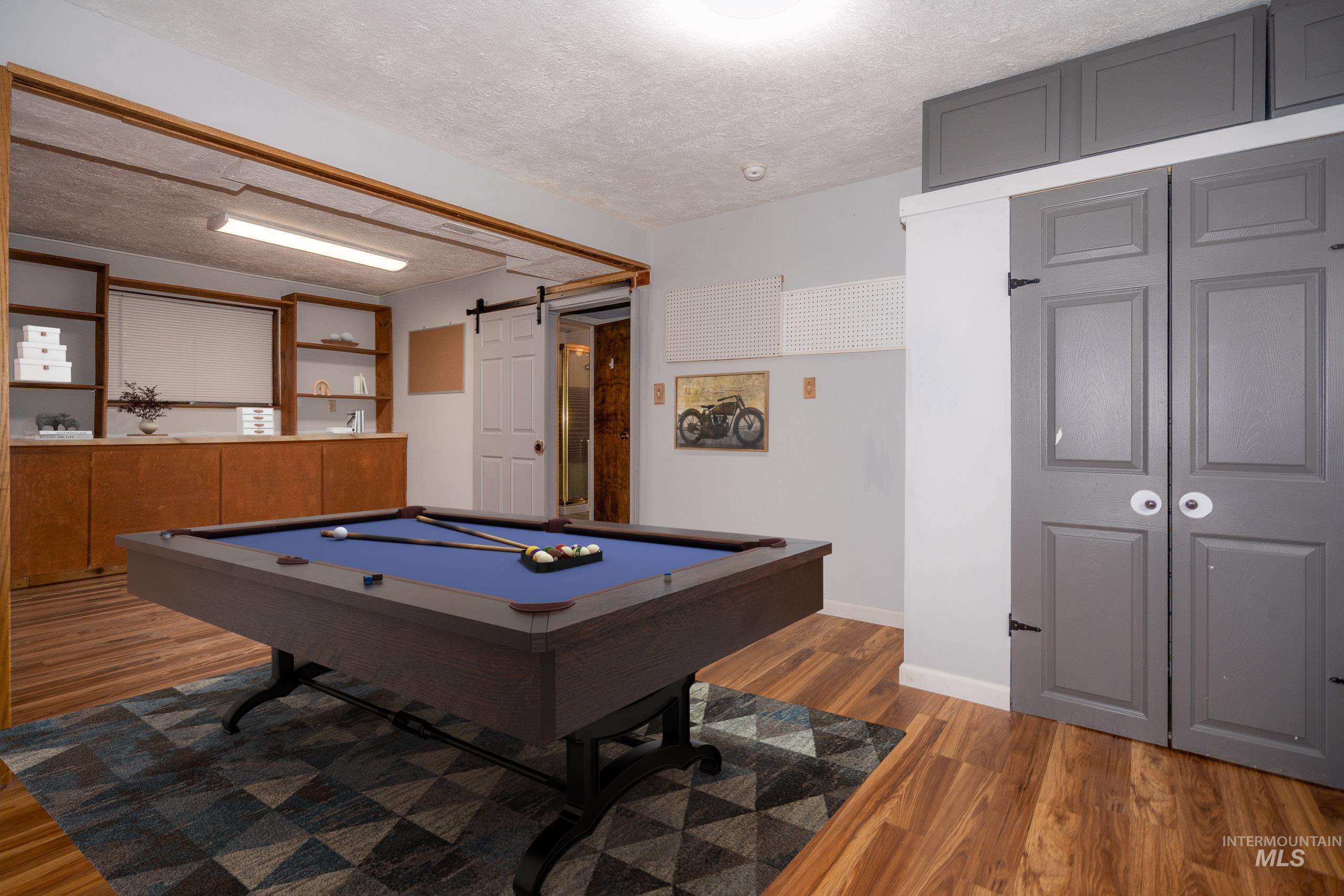 Recreation room with a barn door, a textured ceiling, light wood-style flooring, and billiards table