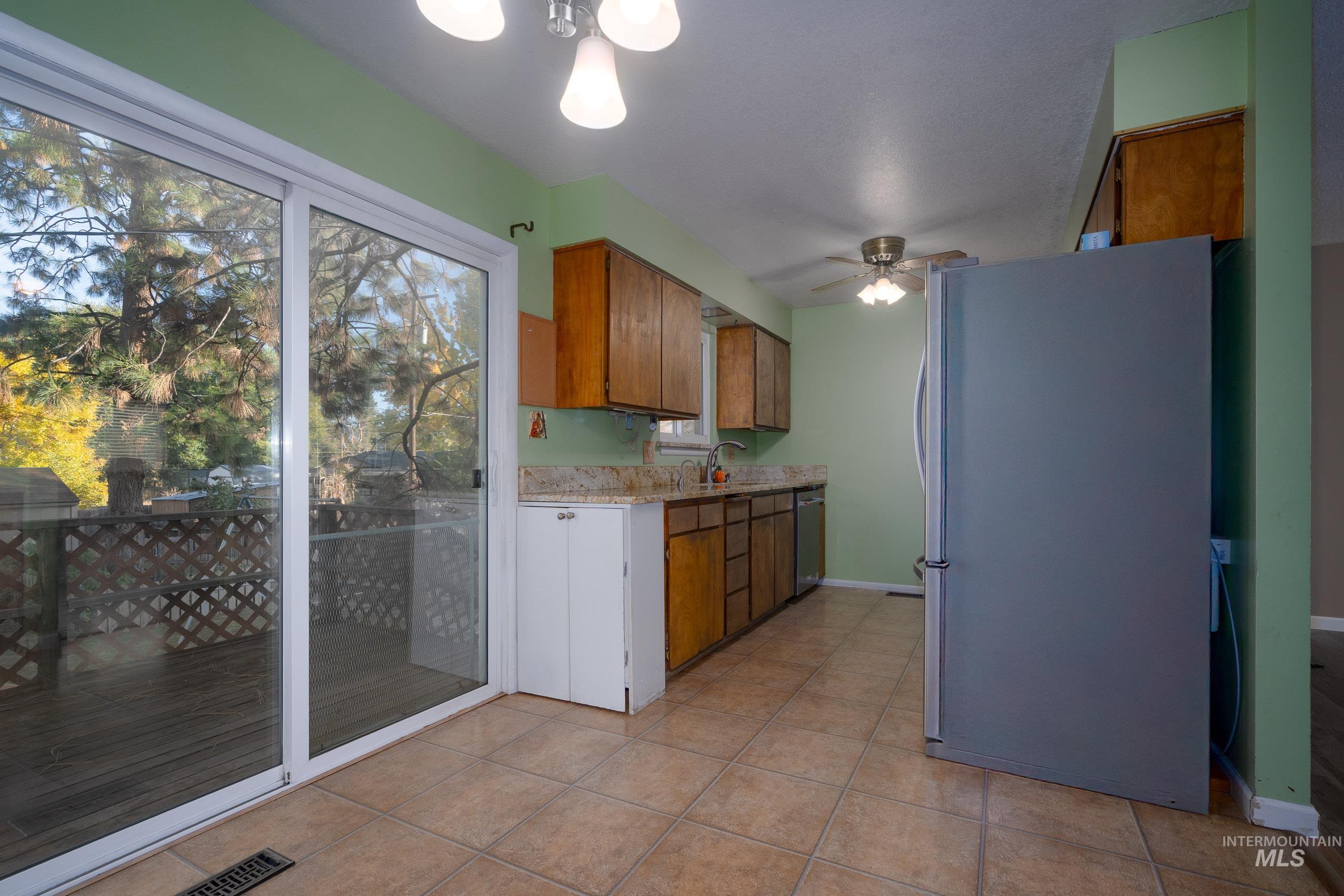Kitchen featuring brown cabinetry, appliances with stainless steel finishes, a ceiling fan, and light tile patterned floors