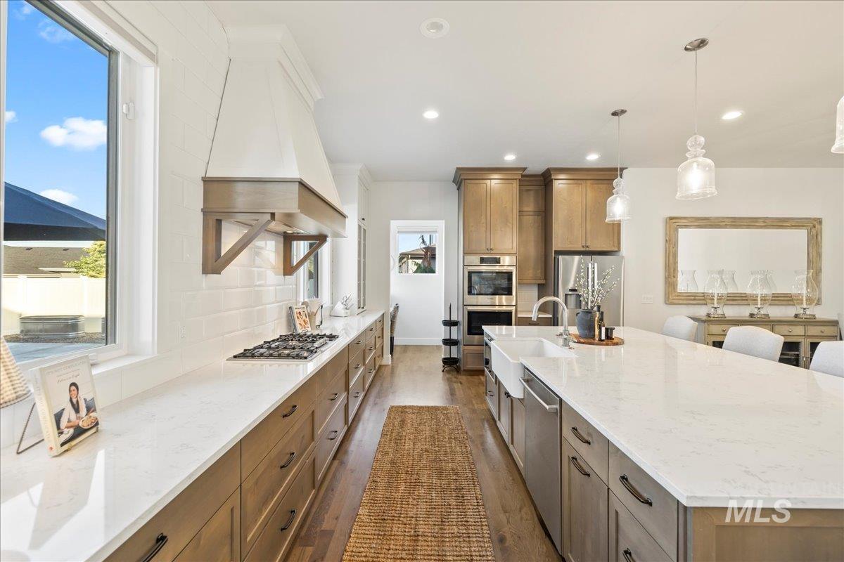 Kitchen with stainless steel appliances, custom exhaust hood, dark wood-style flooring, brown cabinetry, and recessed lighting