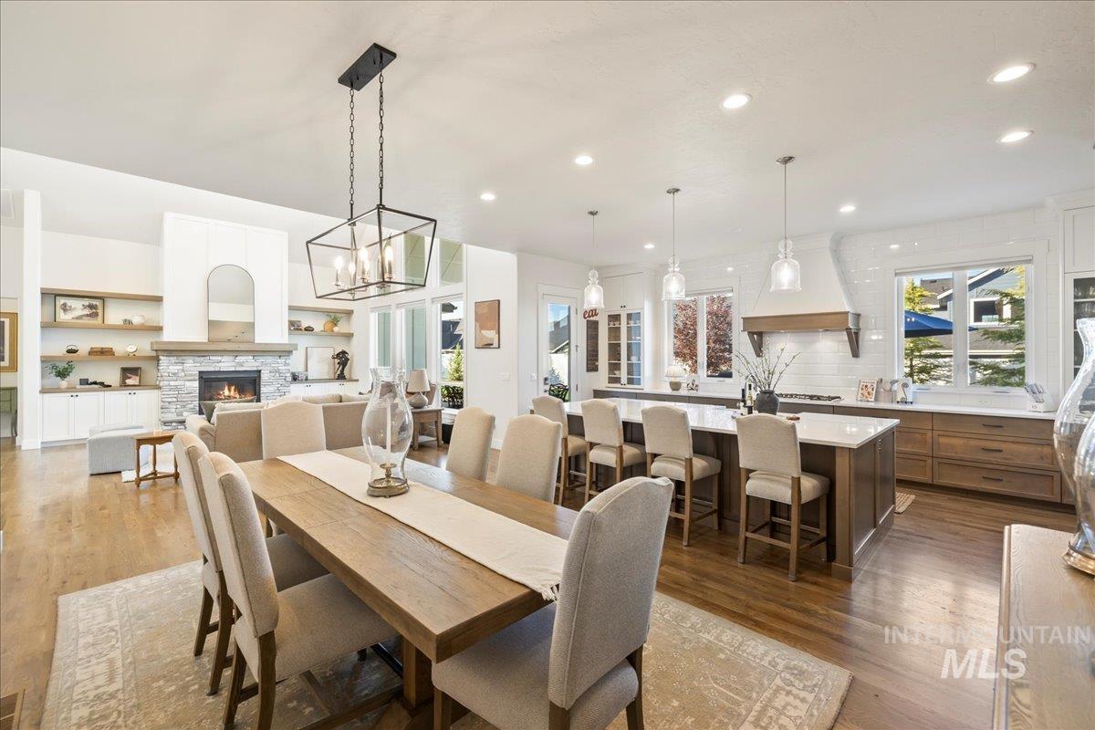 Dining space with wood finished floors, a stone fireplace, and recessed lighting