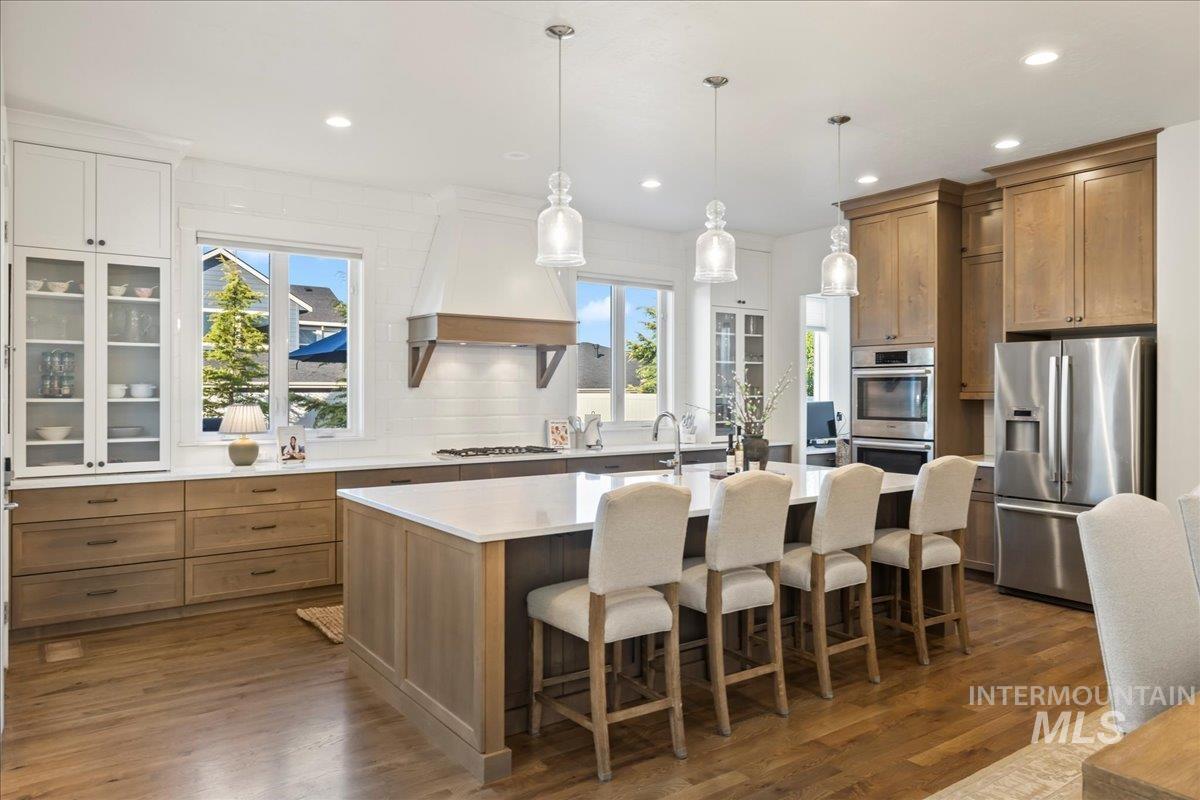 Kitchen featuring appliances with stainless steel finishes, premium range hood, an island with sink, tasteful backsplash, and light countertops
