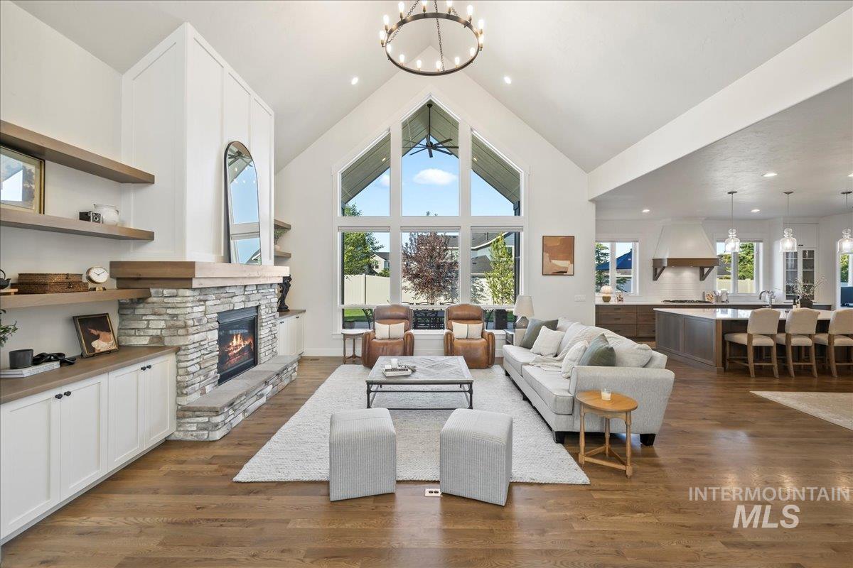 Living area featuring a chandelier, high vaulted ceiling, a stone fireplace, and dark wood-style floors