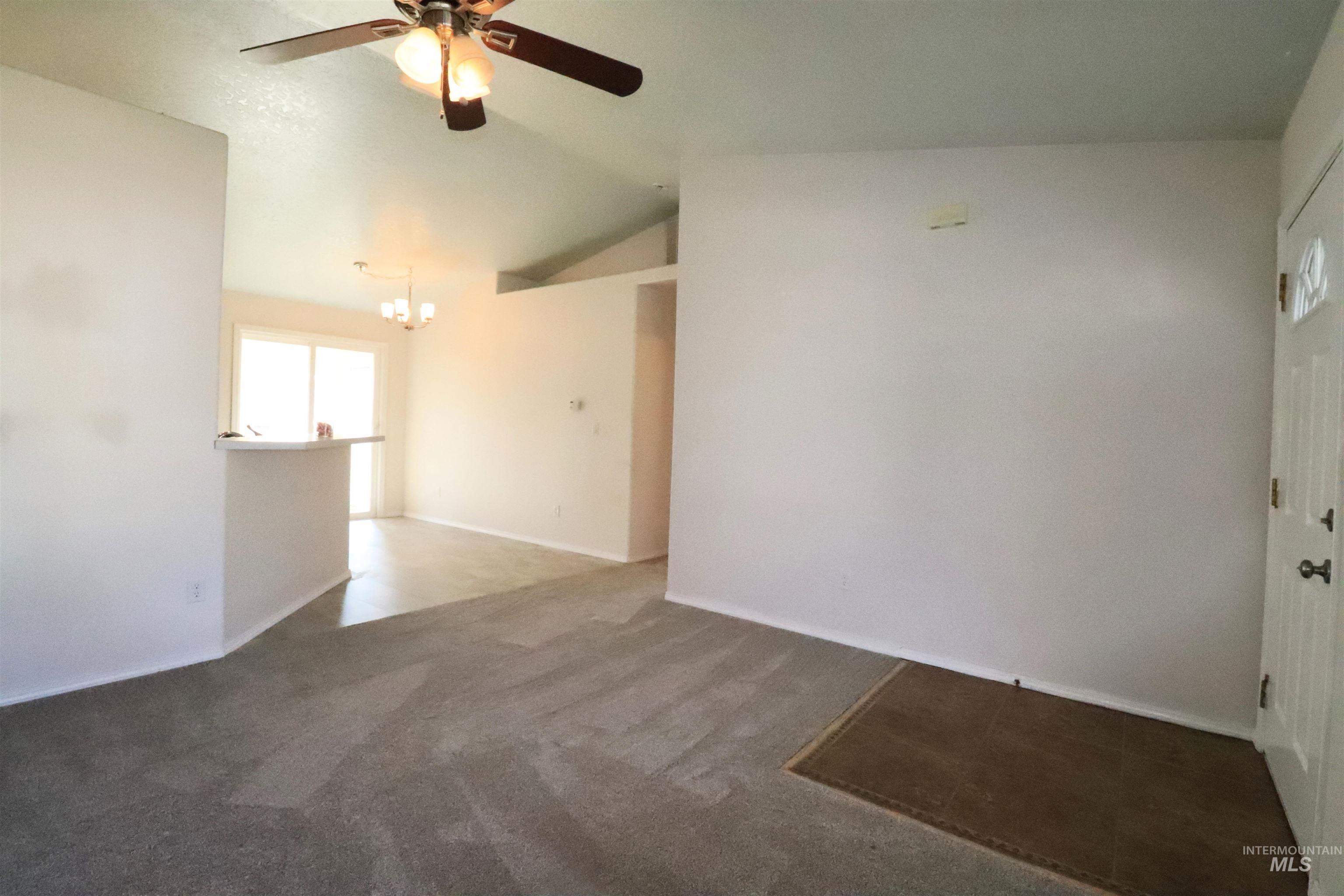 Empty room featuring vaulted ceiling, carpet flooring, a chandelier, and a ceiling fan