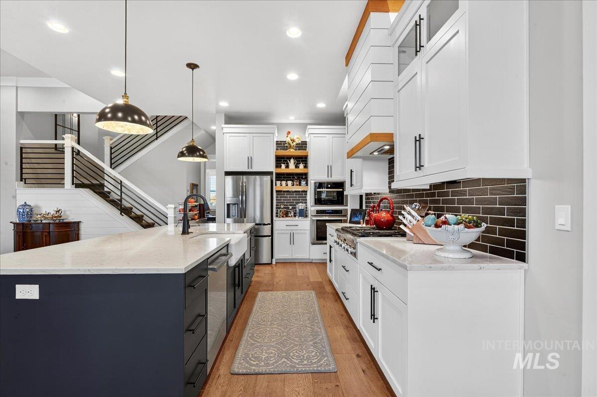 Kitchen with light wood finished floors, hanging light fixtures, light stone counters, open shelves, and stainless steel appliances