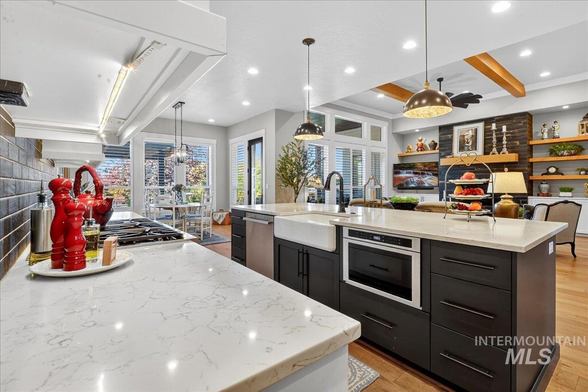 Kitchen with beam ceiling, decorative light fixtures, a kitchen island with sink, light wood-type flooring, and light stone countertops