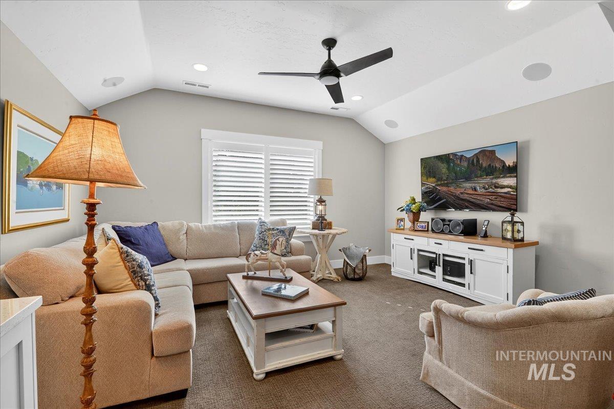 Living area with dark colored carpet, vaulted ceiling, ceiling fan, and recessed lighting
