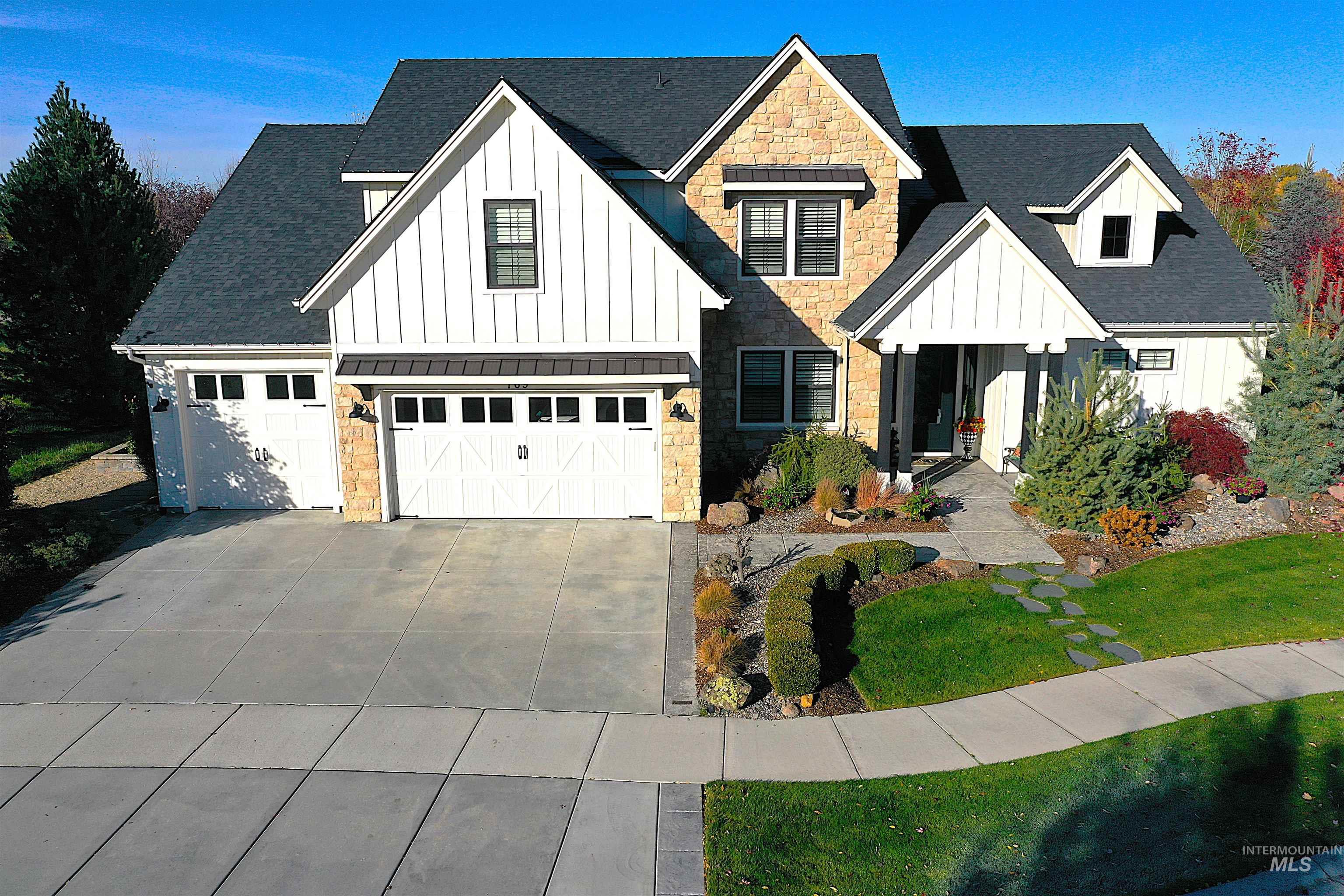 Modern farmhouse style home featuring board and batten siding, stone siding, roof with shingles, and concrete driveway
