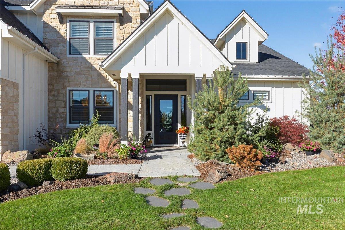 Entrance to property with board and batten siding, stone siding, a yard, and roof with shingles