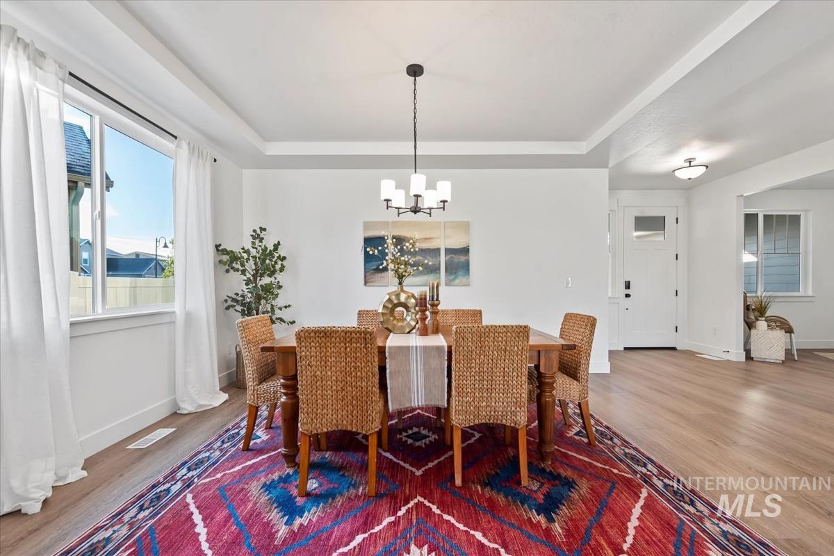 Dining space with a raised ceiling, wood finished floors, and a chandelier