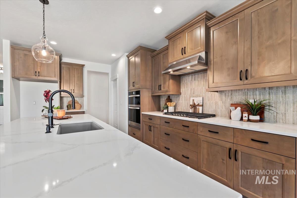 Kitchen featuring brown cabinets, pendant lighting, under cabinet range hood, decorative backsplash, and recessed lighting