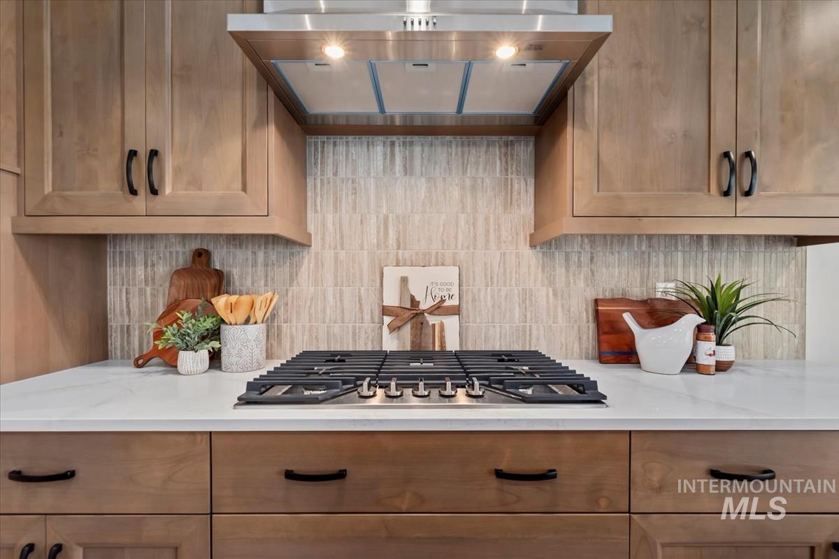 Kitchen with extractor fan, backsplash, stainless steel gas stovetop, and light stone counters