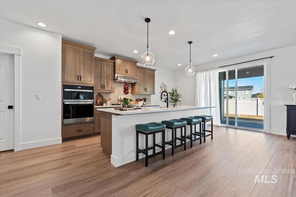 Kitchen featuring brown cabinetry, a breakfast bar area, decorative light fixtures, a kitchen island with sink, and recessed lighting