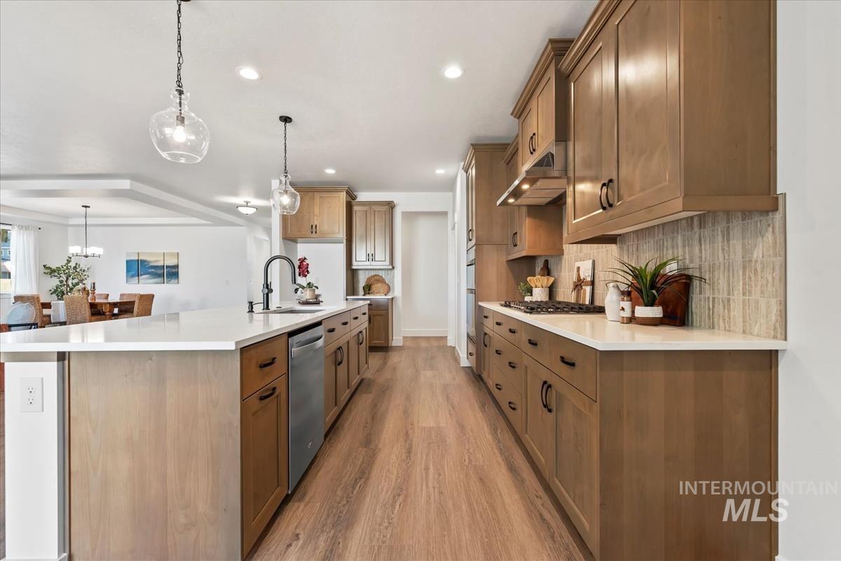 Kitchen featuring a spacious island, brown cabinets, hanging light fixtures, light wood-type flooring, and recessed lighting