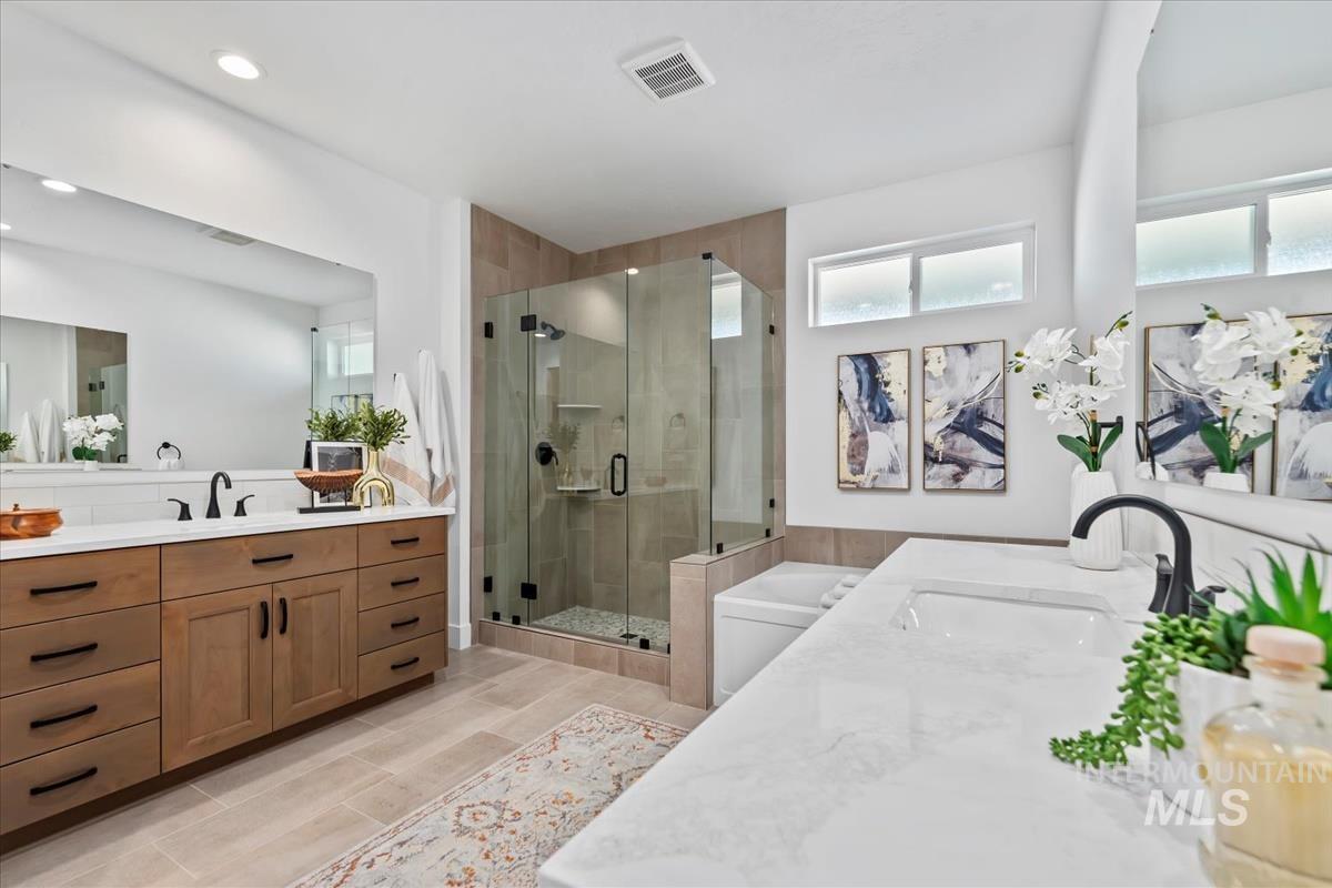 Bathroom featuring two vanities, a stall shower, a tub to relax in, and plenty of natural light
