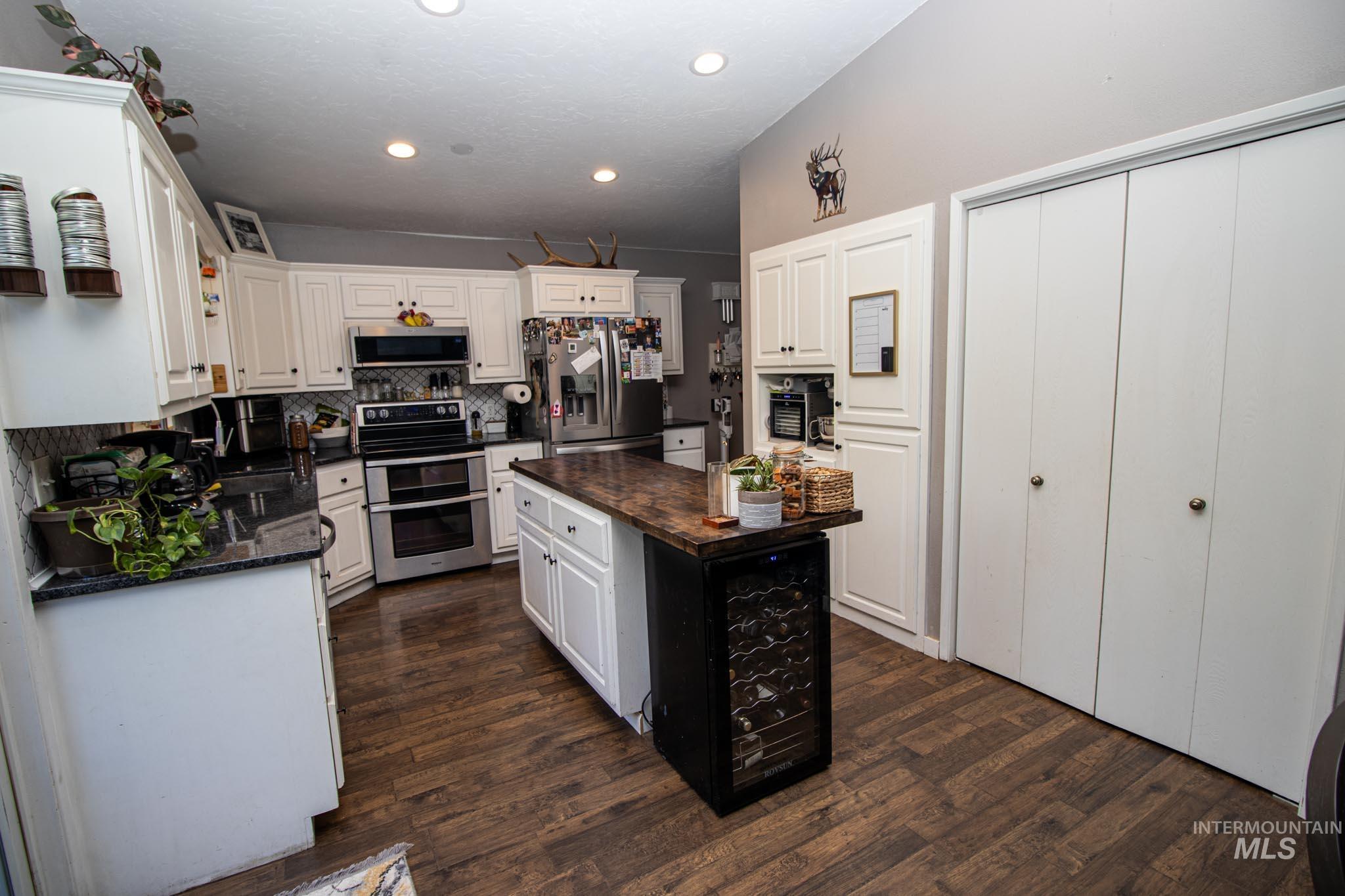Kitchen with stainless steel appliances, a kitchen island, dark wood finished floors, decorative backsplash, and white cabinetry