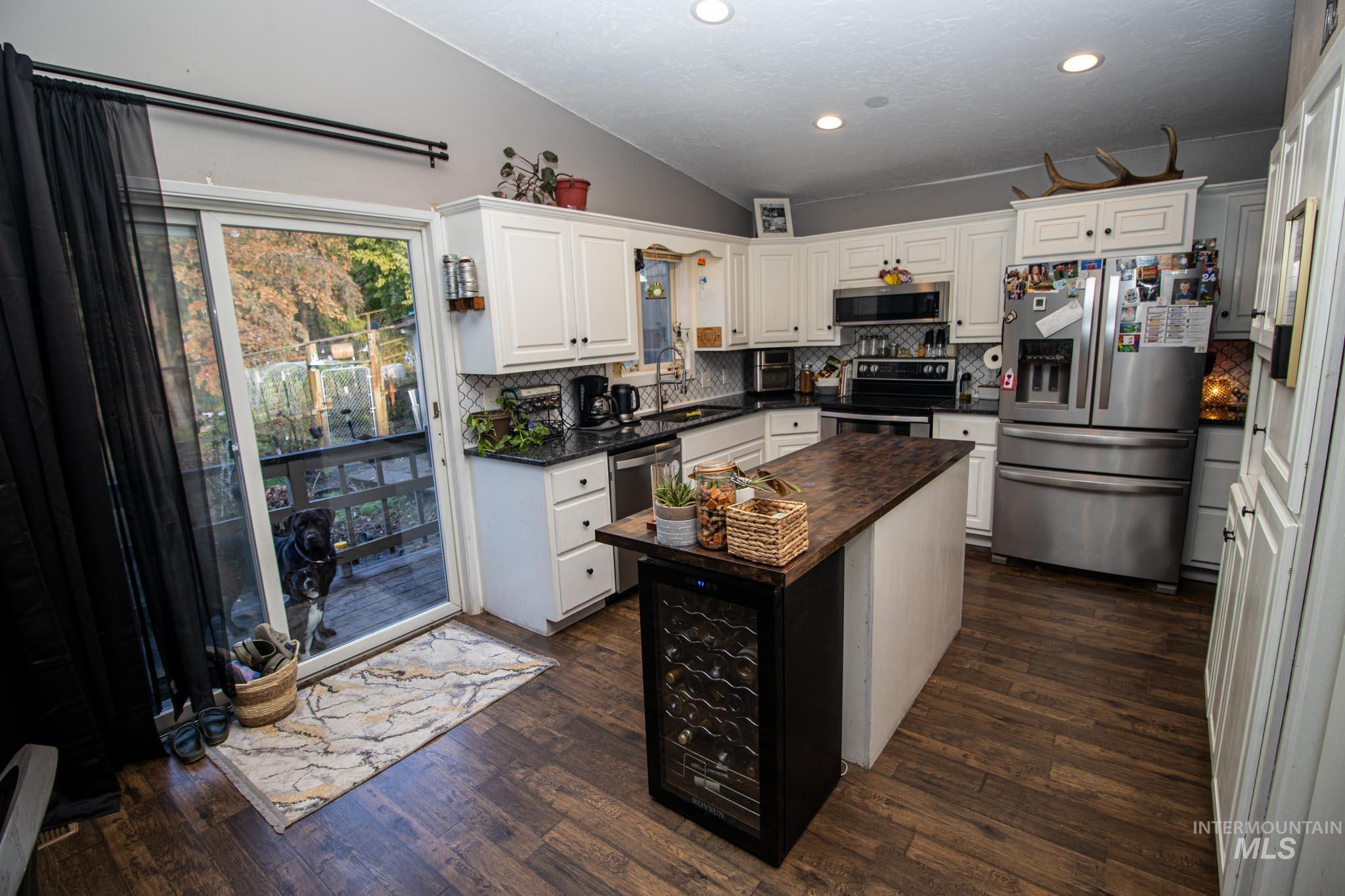 Kitchen with appliances with stainless steel finishes, backsplash, dark wood-style floors, white cabinetry, and vaulted ceiling