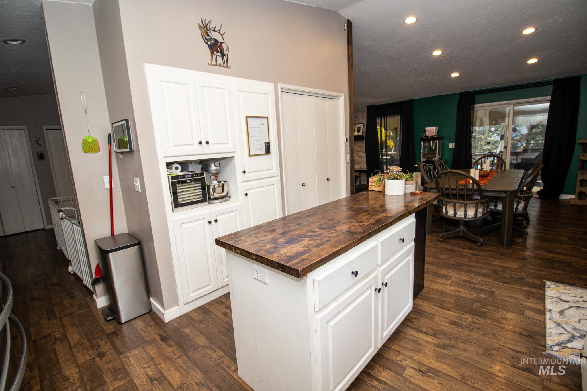 Kitchen with butcher block counters, white cabinets, dark wood-type flooring, recessed lighting, and a center island