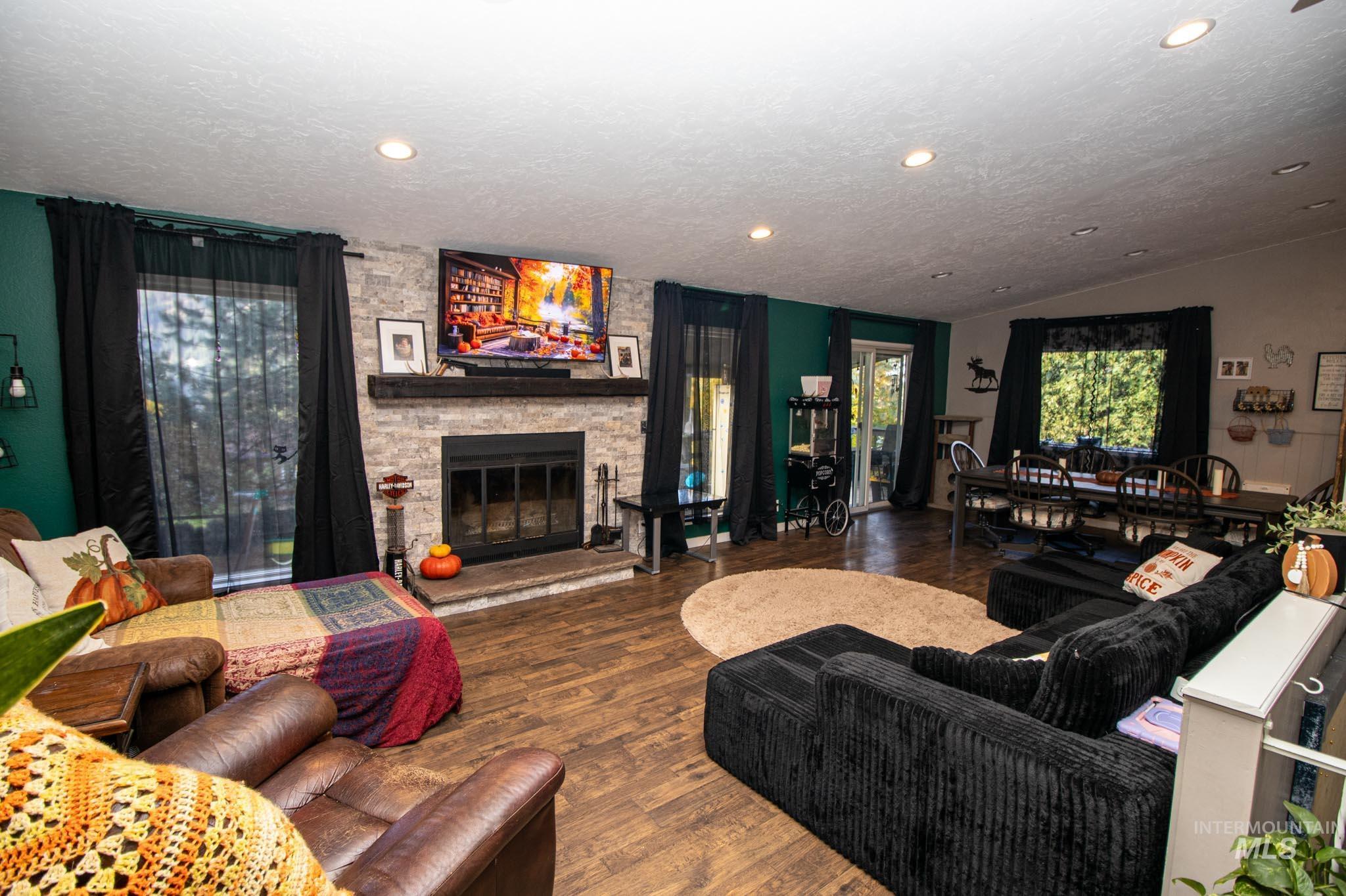 Living area featuring a stone fireplace, lofted ceiling, dark wood-style floors, a textured ceiling, and recessed lighting