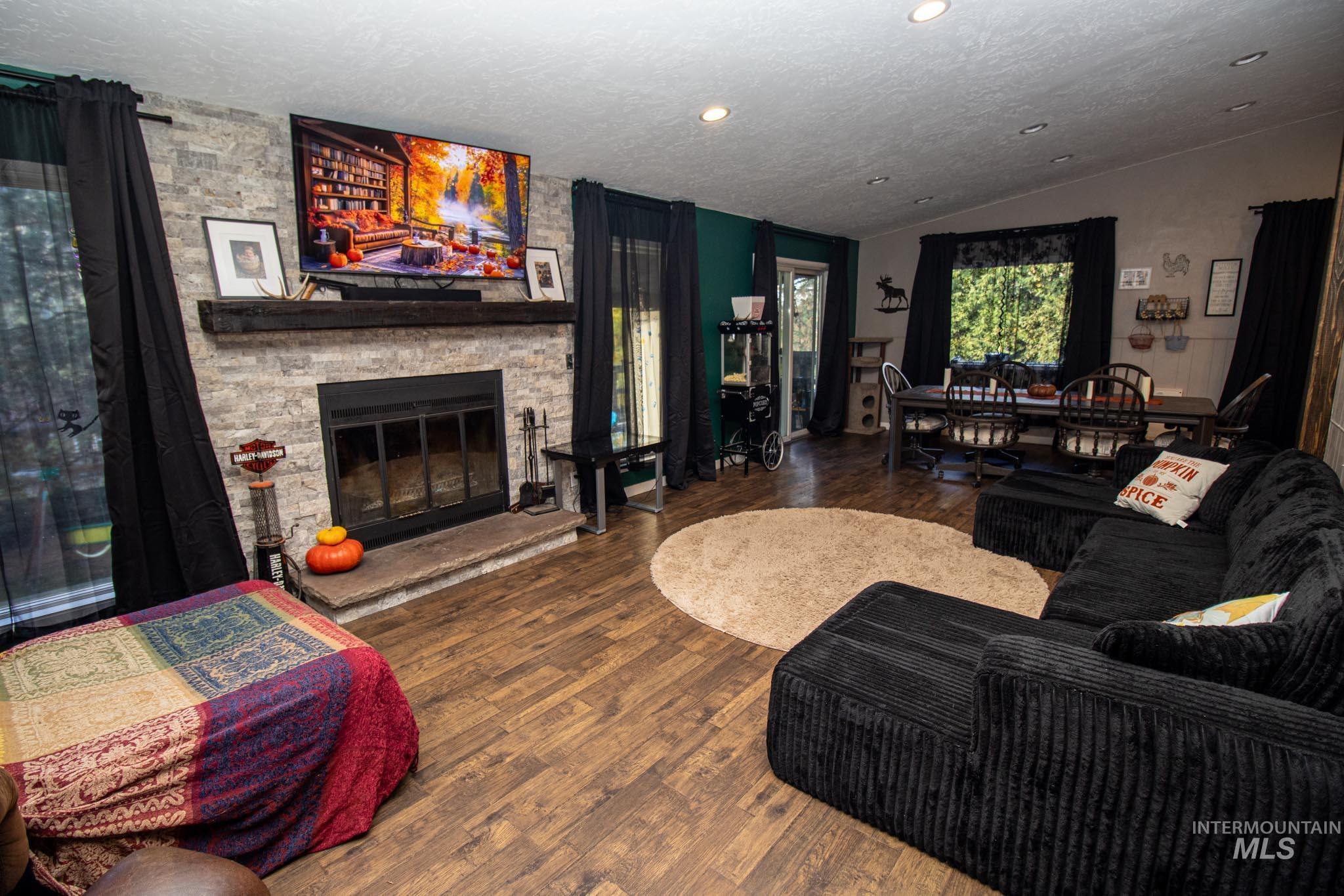 Living room featuring vaulted ceiling, wood finished floors, a textured ceiling, a stone fireplace, and recessed lighting