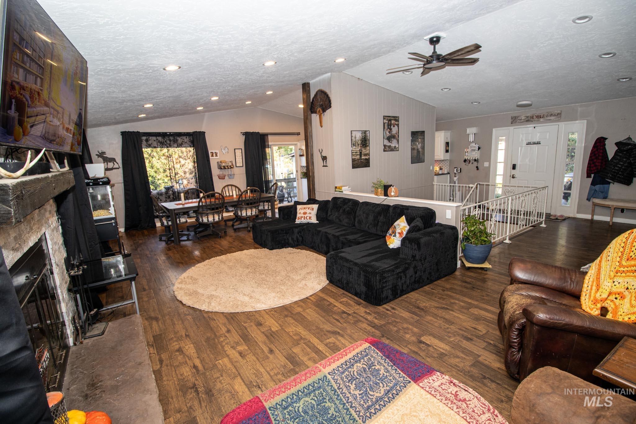 Living area featuring dark wood finished floors, vaulted ceiling, a fireplace, a textured ceiling, and ceiling fan