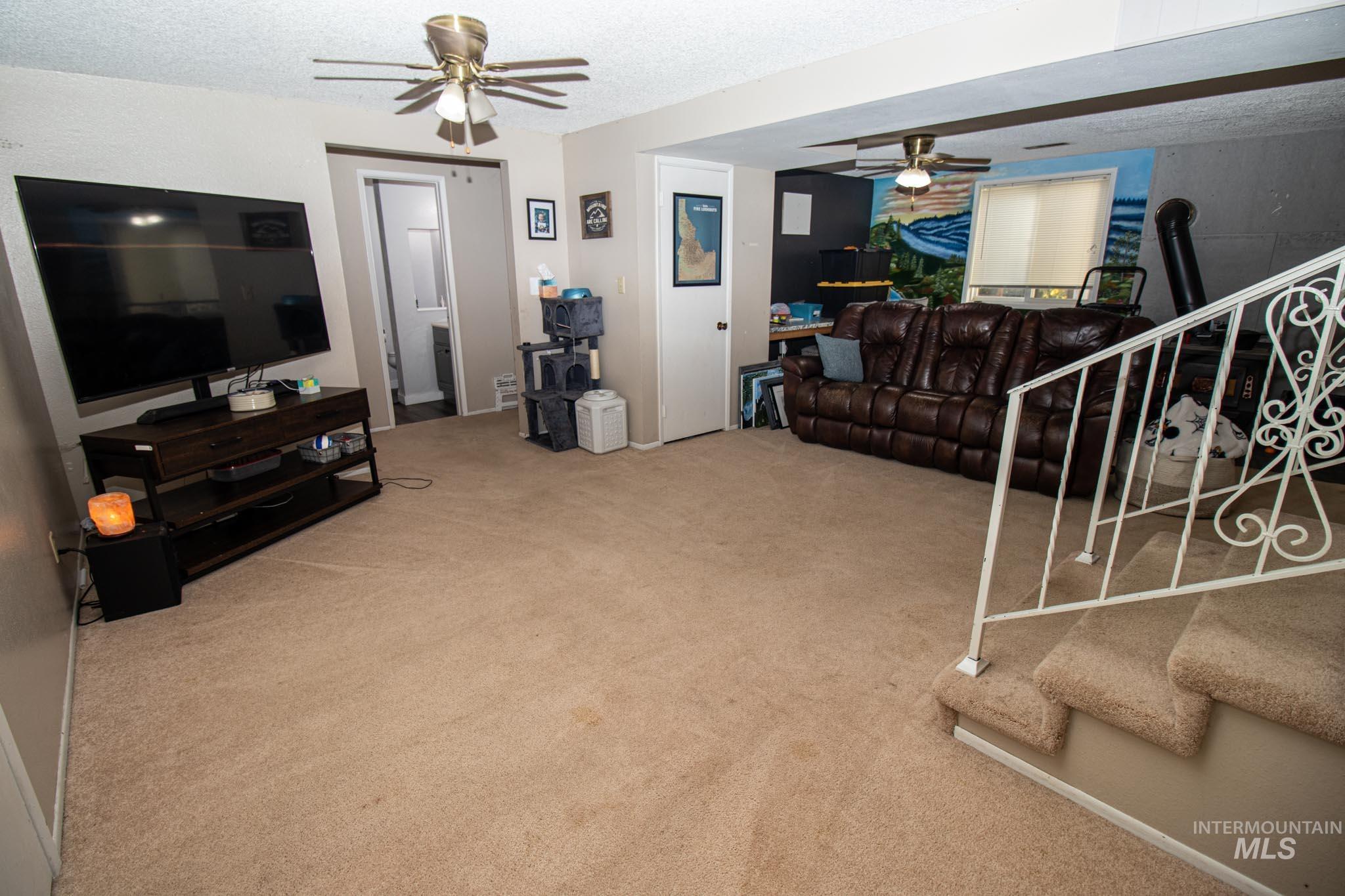 Living area featuring ceiling fan, light carpet, stairs, and a textured ceiling