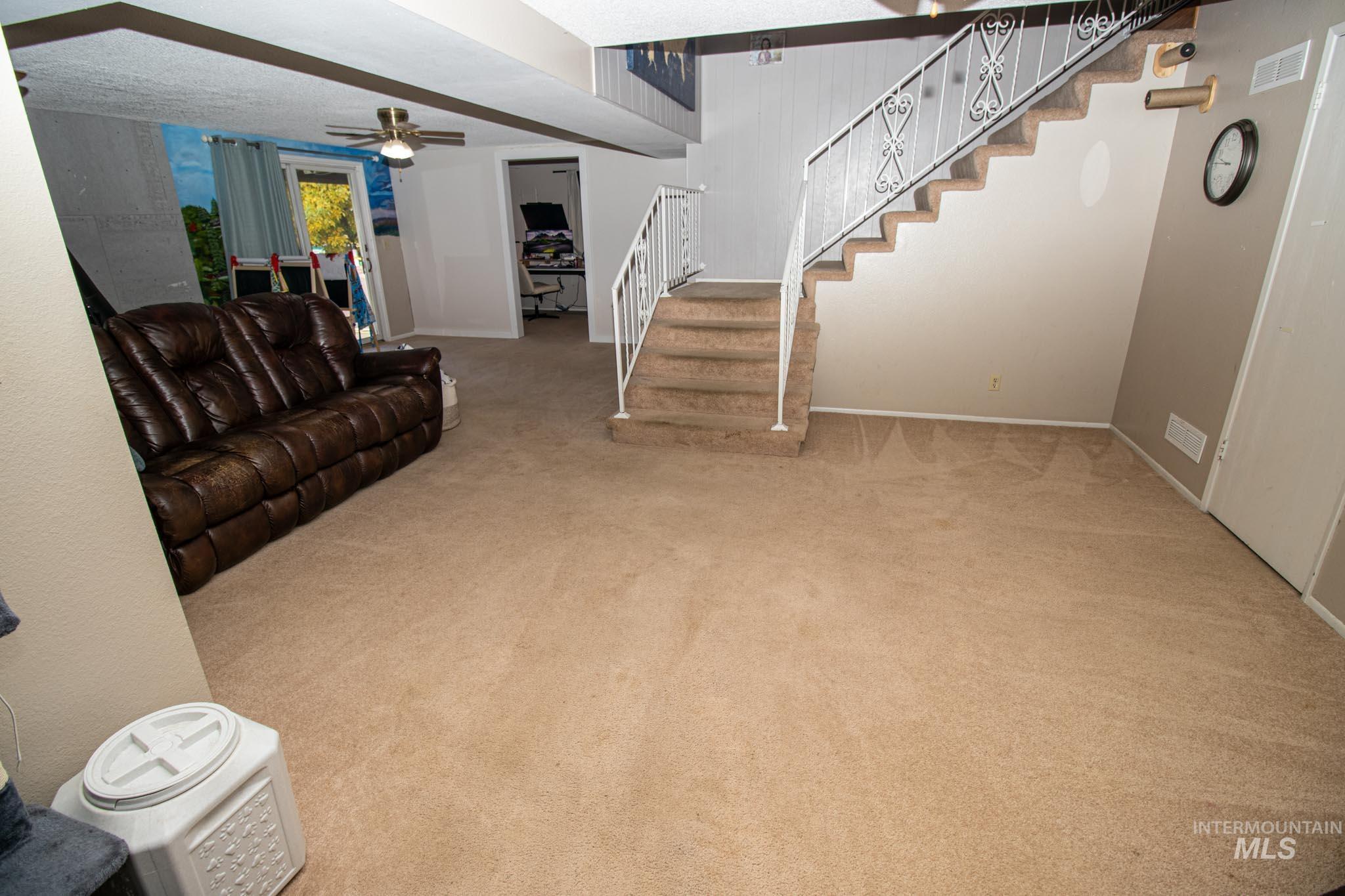 Living room featuring light colored carpet, stairs, a ceiling fan, and a textured ceiling