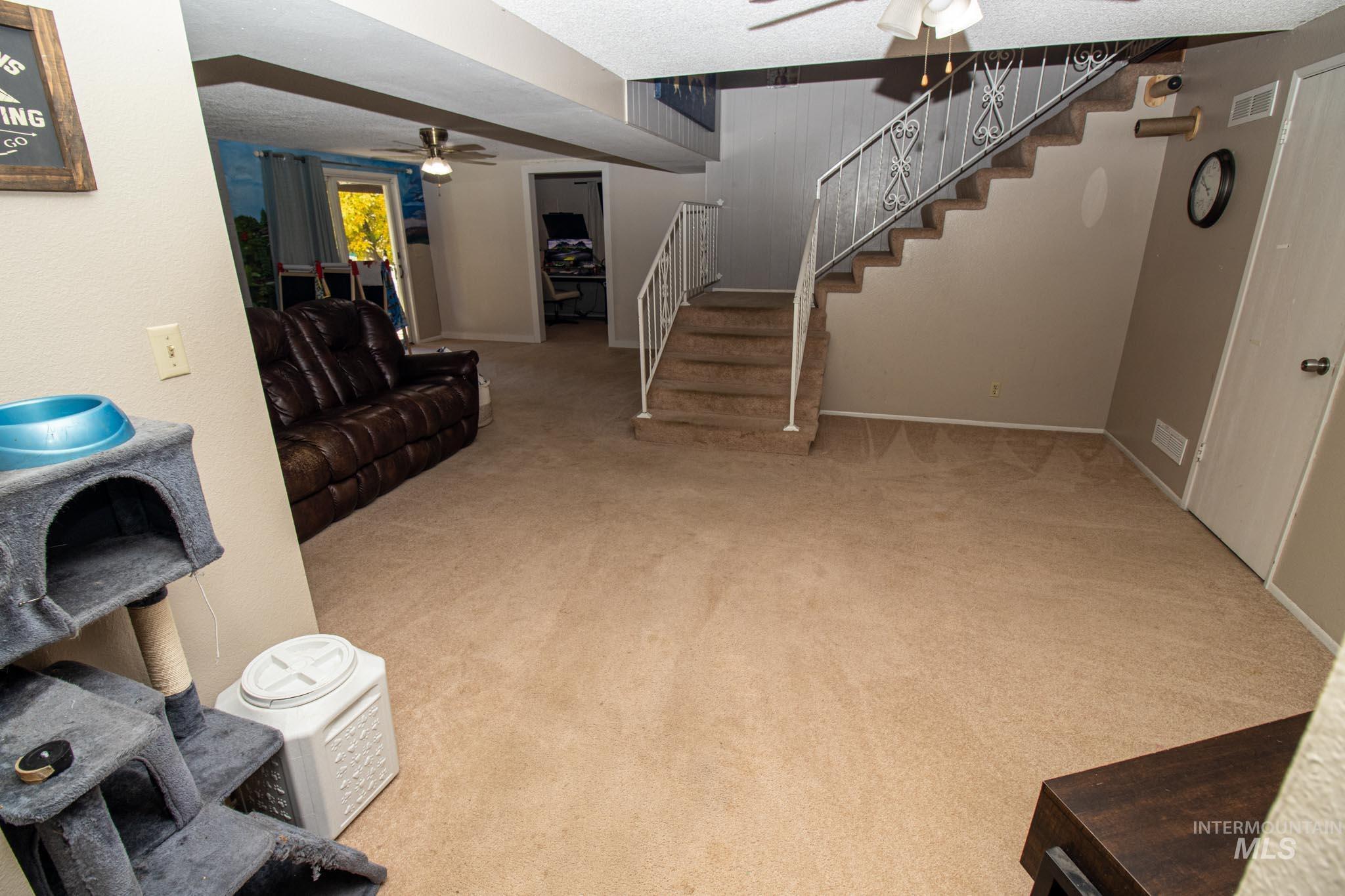 Living area with ceiling fan, light colored carpet, a textured ceiling, and stairs